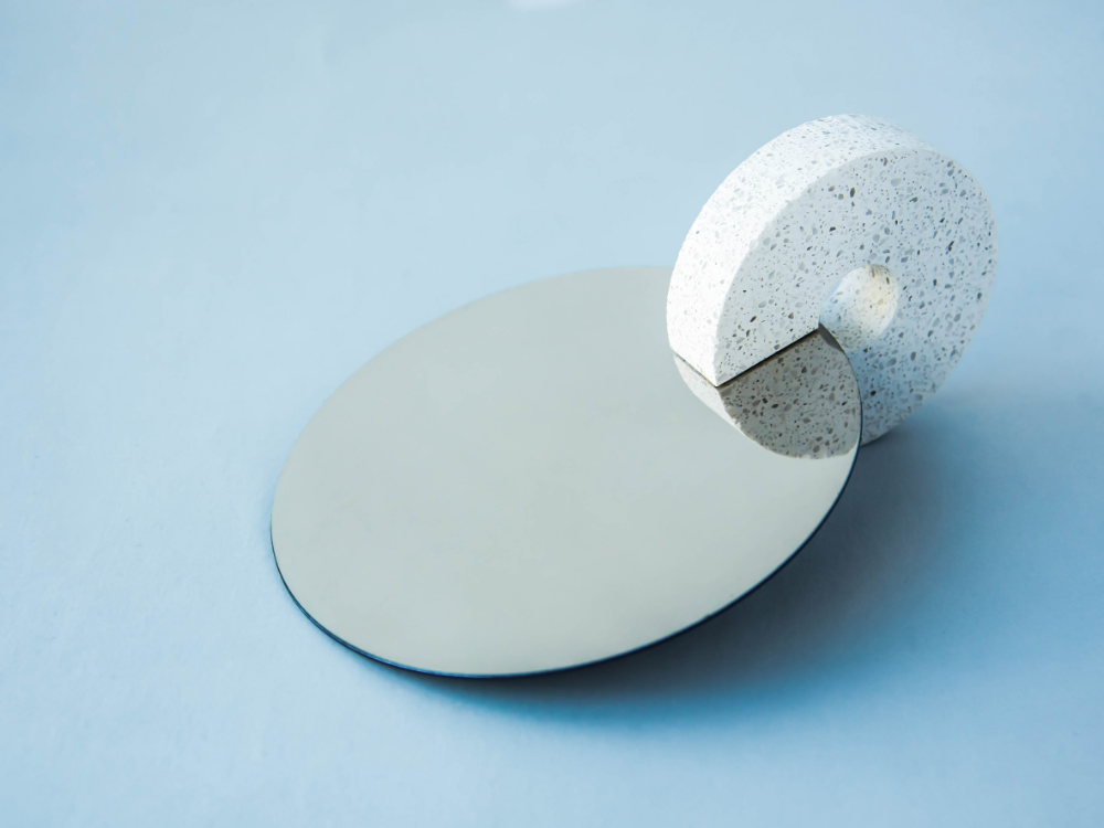 A round mirror with a terrazzo-patterned cylindrical stand on a light blue surface.