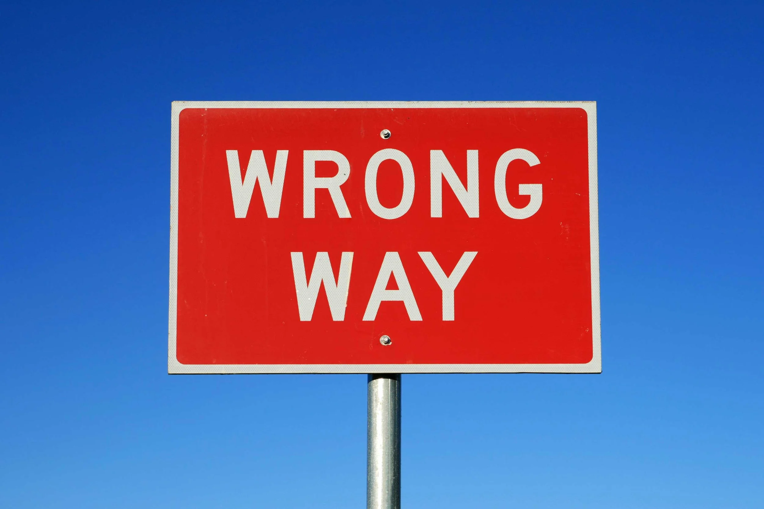 "Wrong Way" road sign against a clear blue sky.