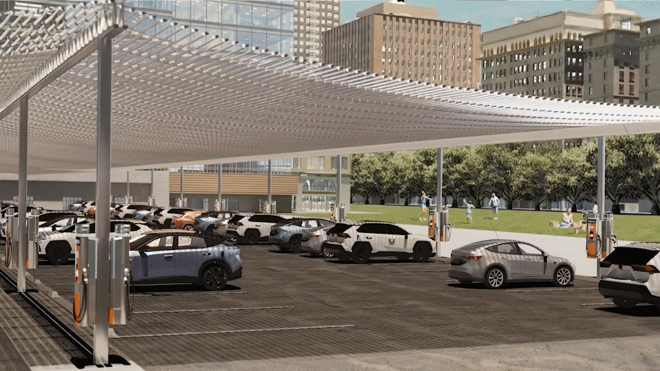 Electric car charging station in a parking lot with multiple cars plugged in, surrounded by city buildings and people walking in the park nearby.