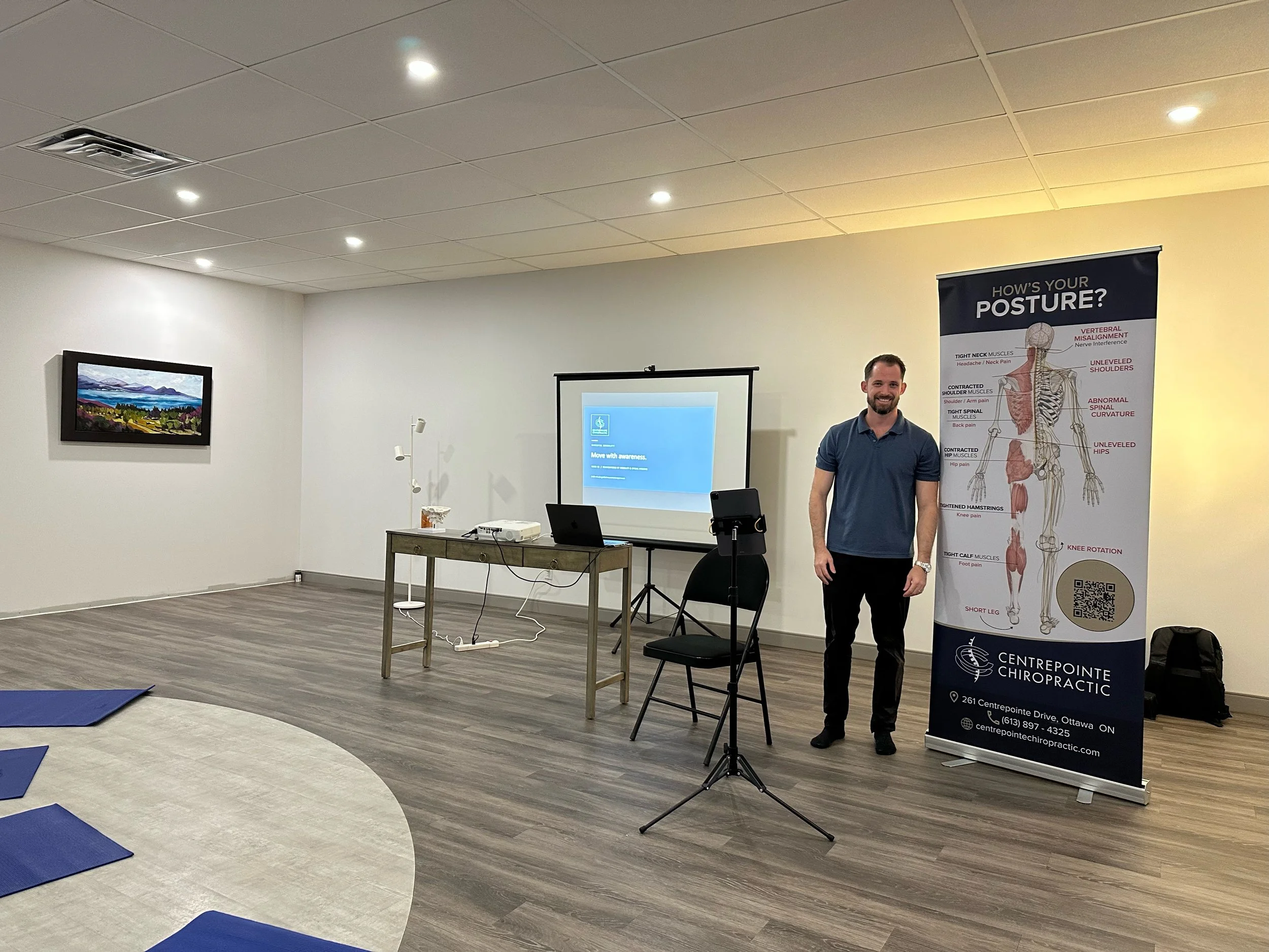 Chiropractor standing beside a posture education banner and presentation setup in a wellness studio.