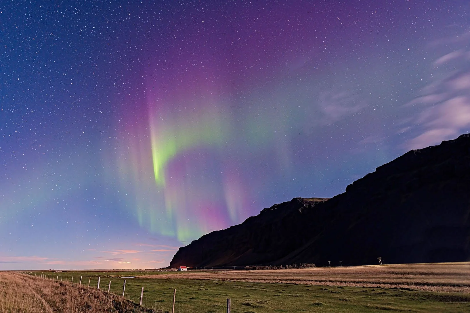 Northern lights above a remote mountain in Iceland with a red-roofed house, captured by Dean Best for the Best Calming Relaxation project.