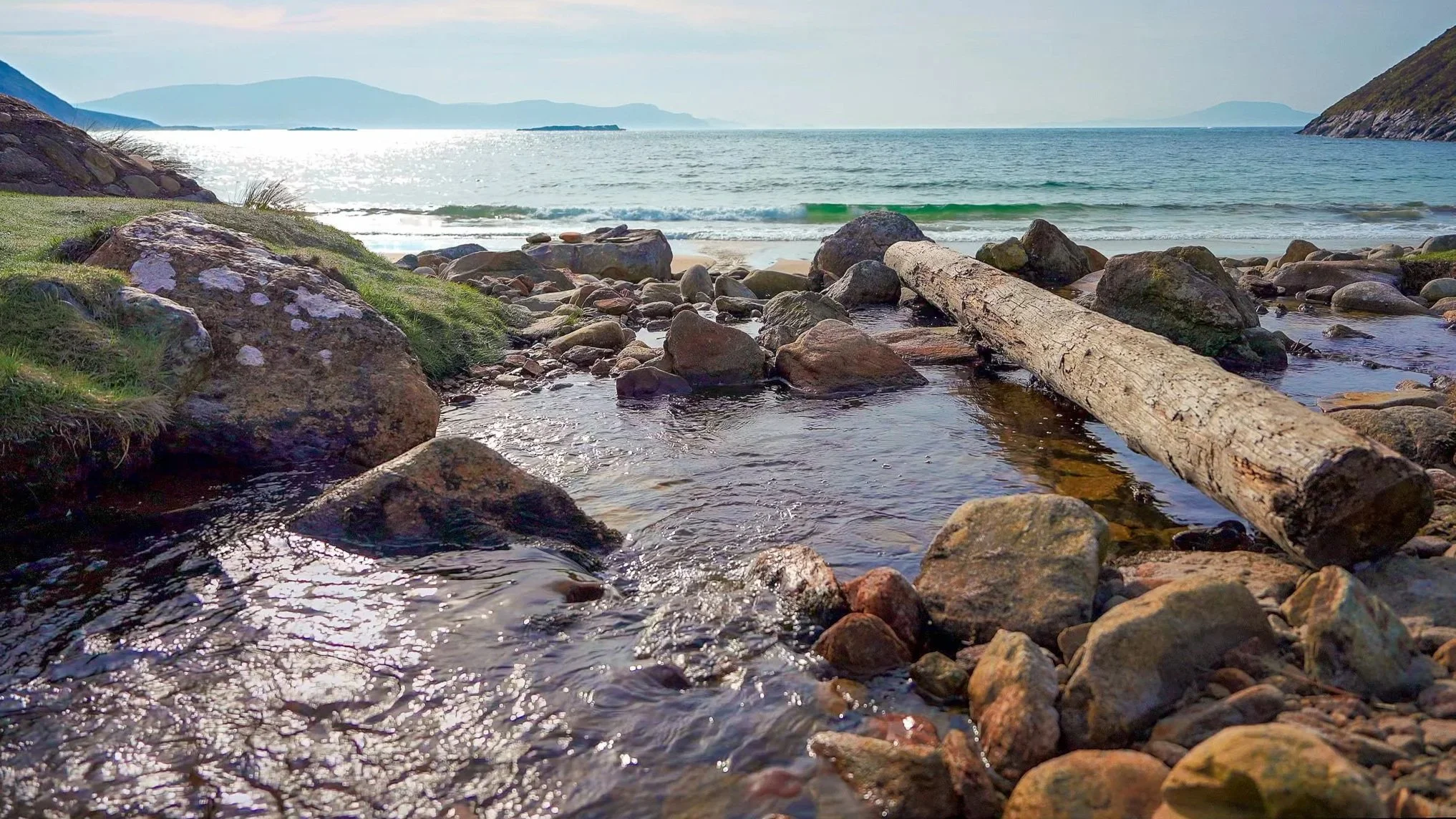 Coastal stream flowing over rocks and driftwood toward the sea in Ireland from the 3-hour calming piano music video Where the Stream Meets the Sea by Dean Best.