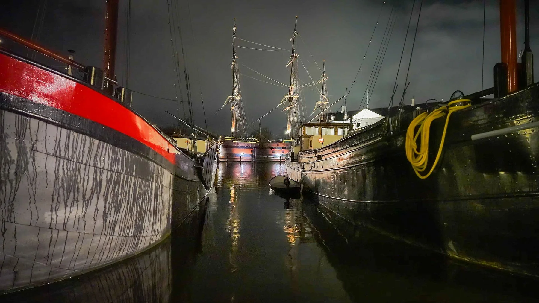 Historic ships resting in an Amsterdam harbor at night with warm lights and water reflections from the 3-hour calming piano music video Stillpoint by Dean Best.