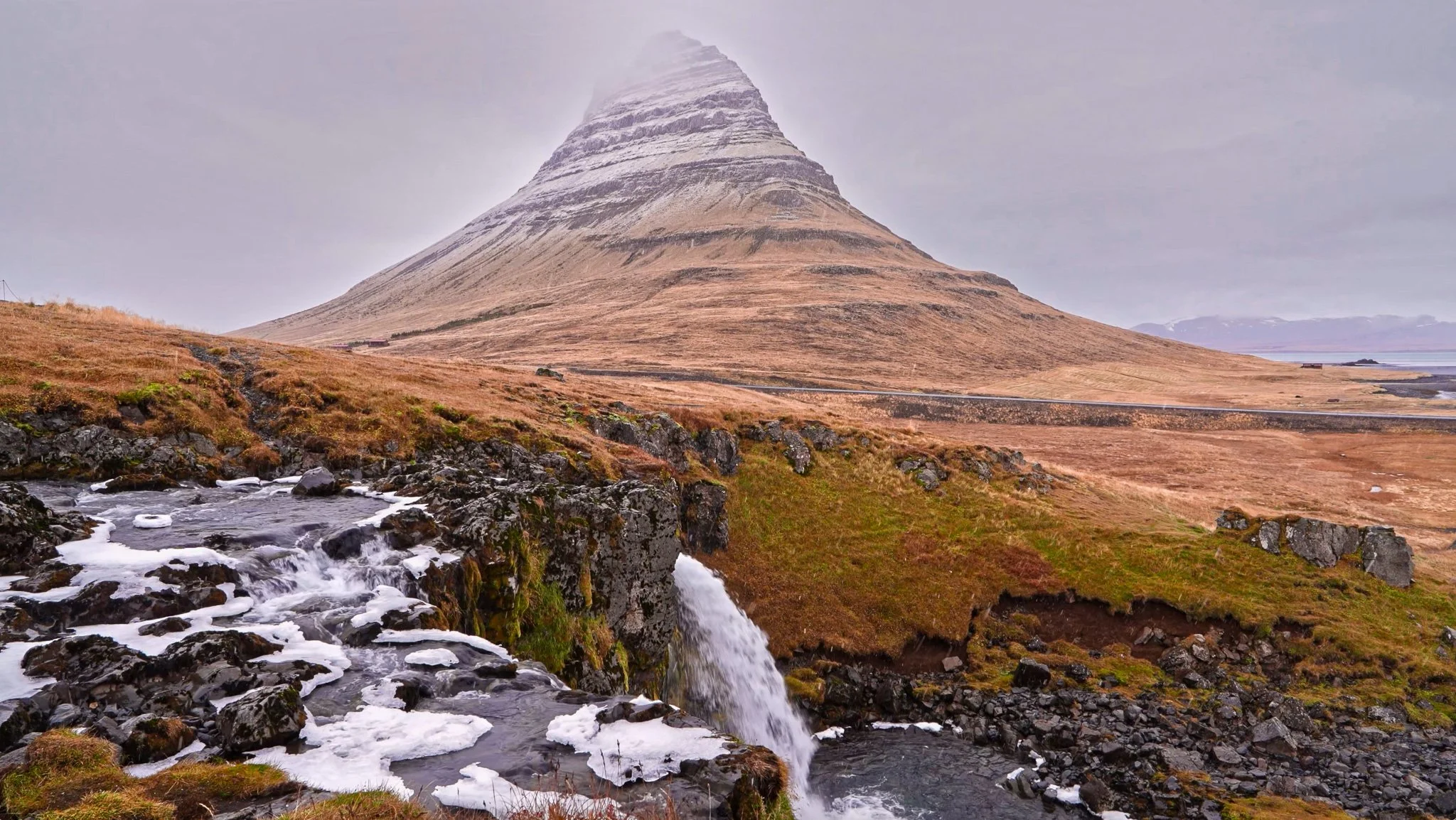 Misty Kirkjufell waterfall in Iceland with soft mountain clouds and rocky flowing water, filmed by Dean Best for Relax With Dean.