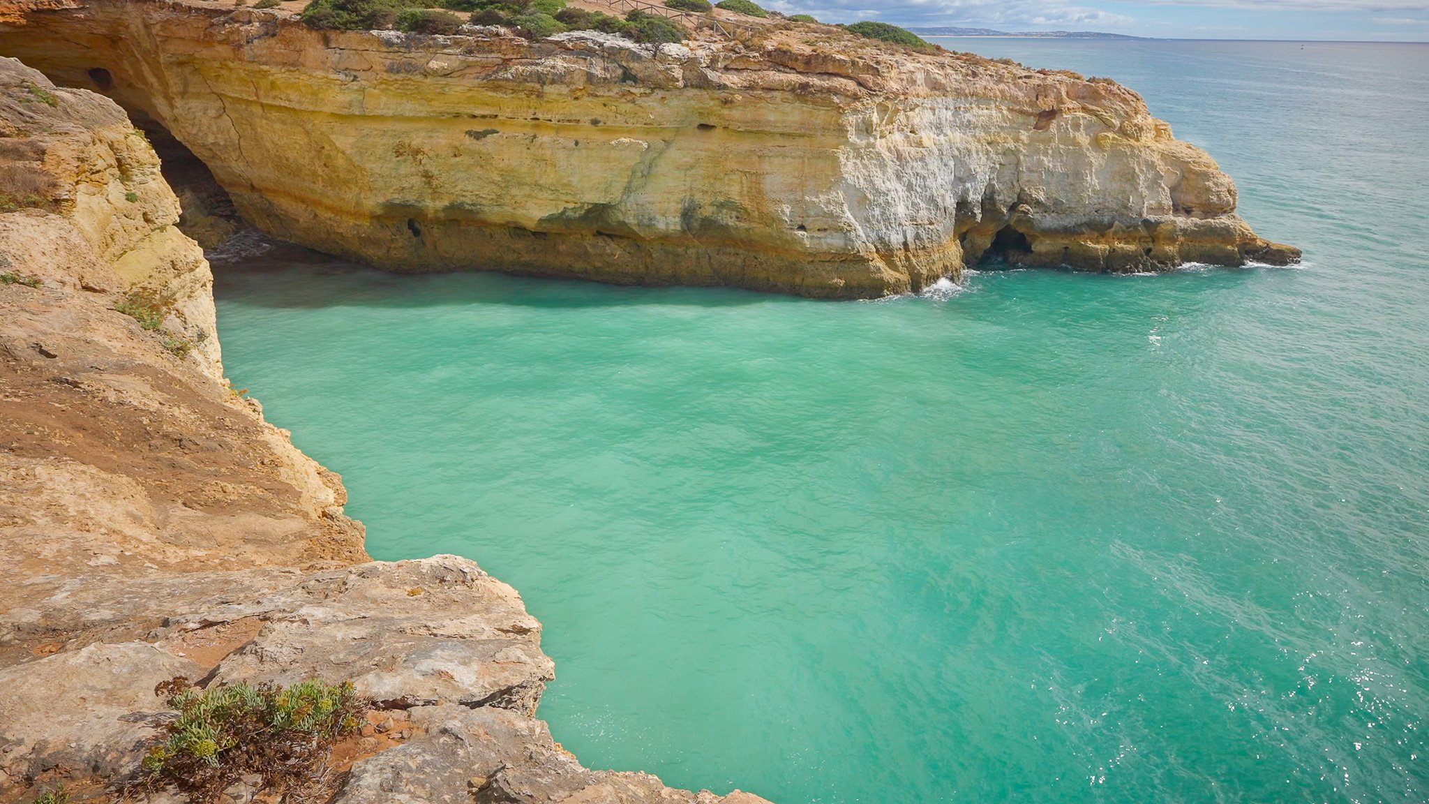 Turquoise ocean water beside sunlit sea cliffs in Algarve, Portugal with peaceful coastal scenery and calm sea movement.