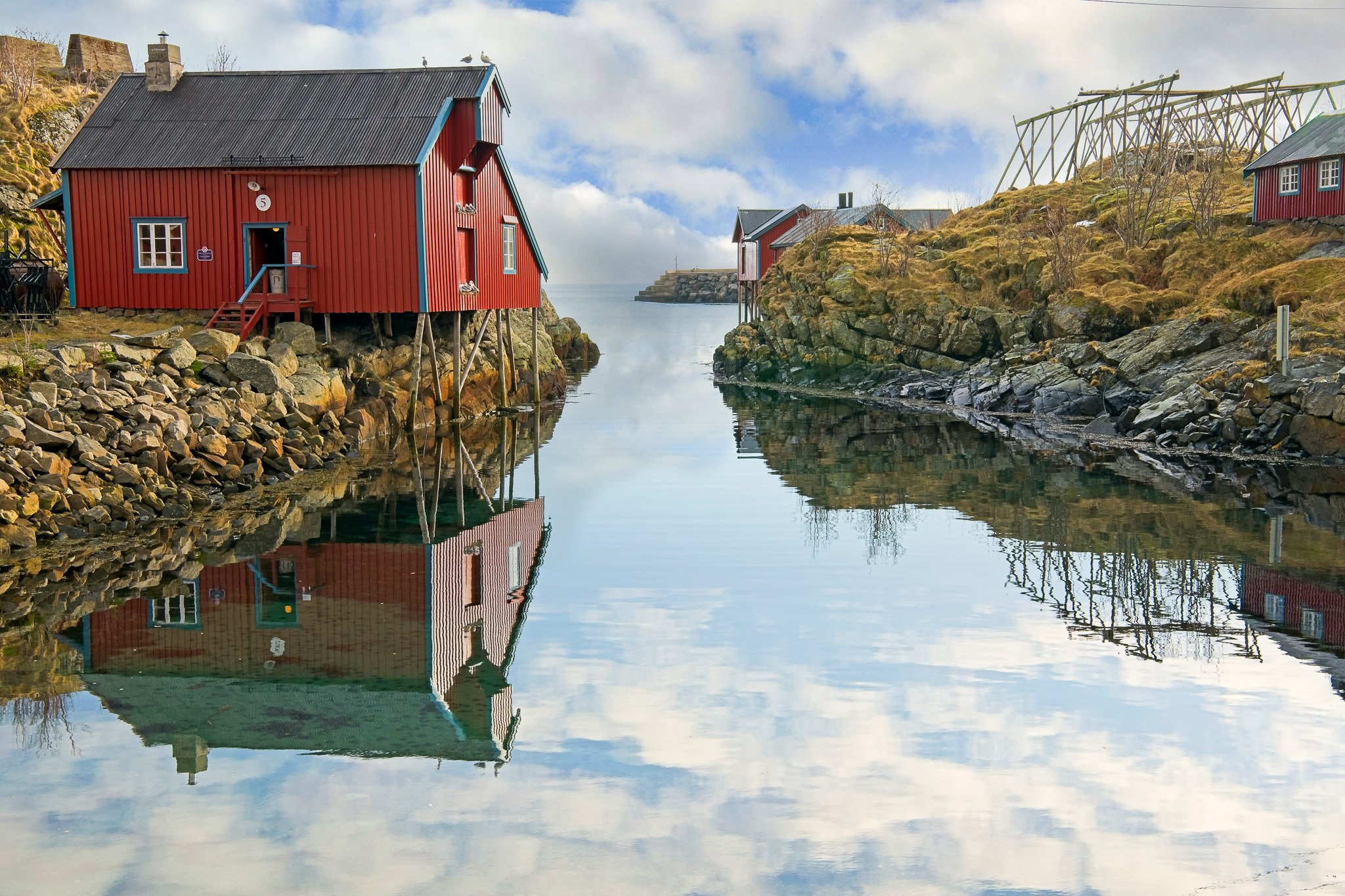 Red coastal cabins reflected in still fjord water in Lofoten, Norway, featured in the Echoes of the Fjord 3-hour calming piano video by Dean Best.