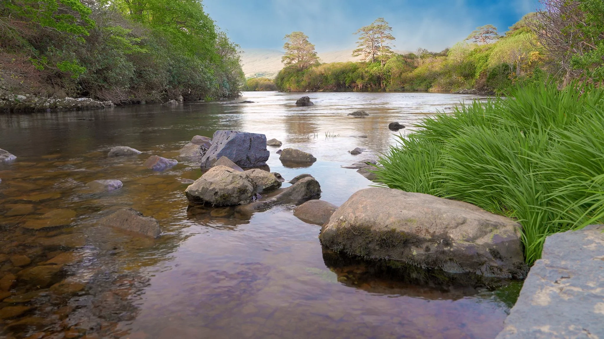 Gentle river flowing around smooth stones in Ireland with soft natural light and peaceful green scenery.