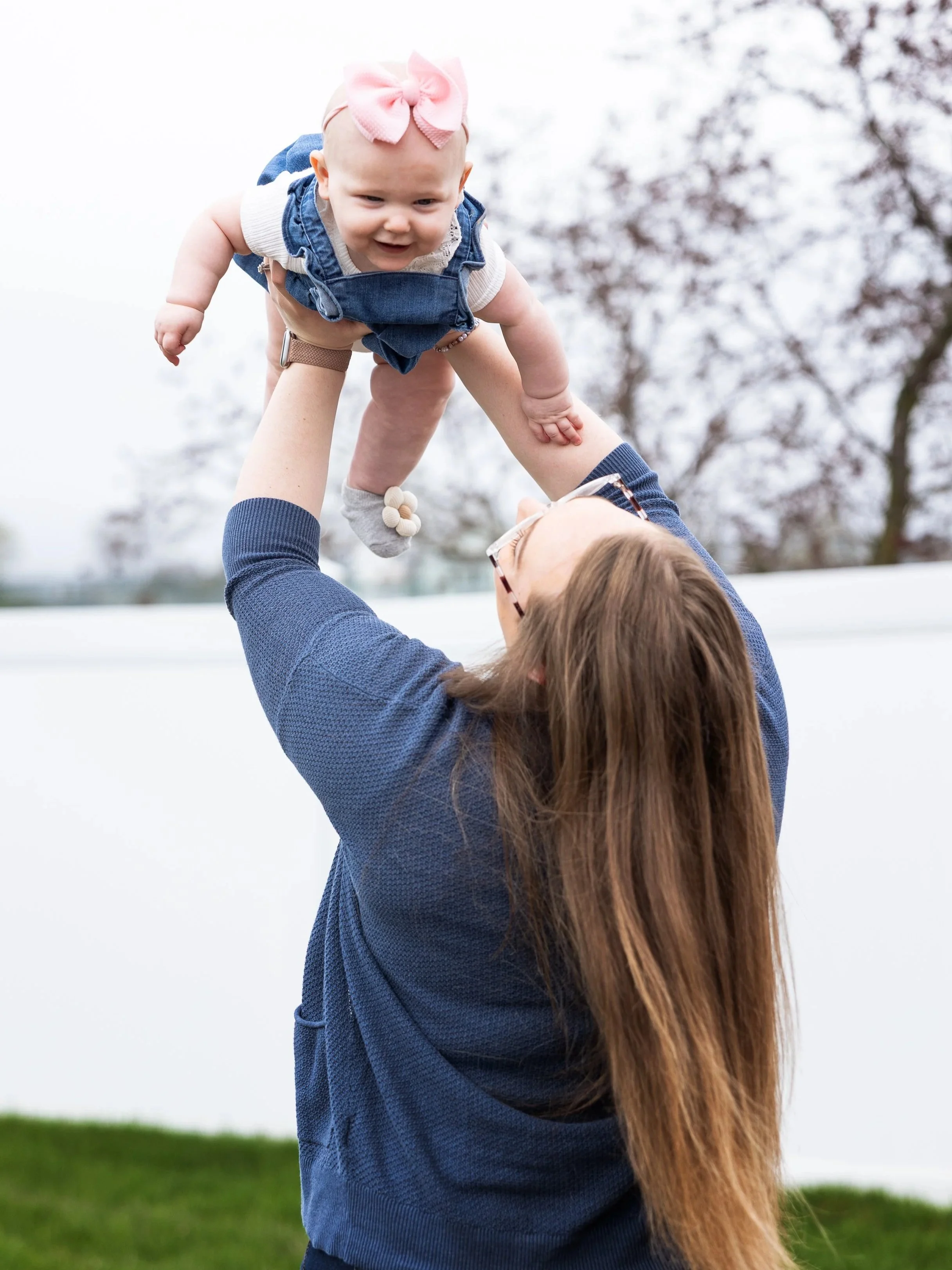 Mother lifting baby girl into the air during outdoor lifestyle family portrait session