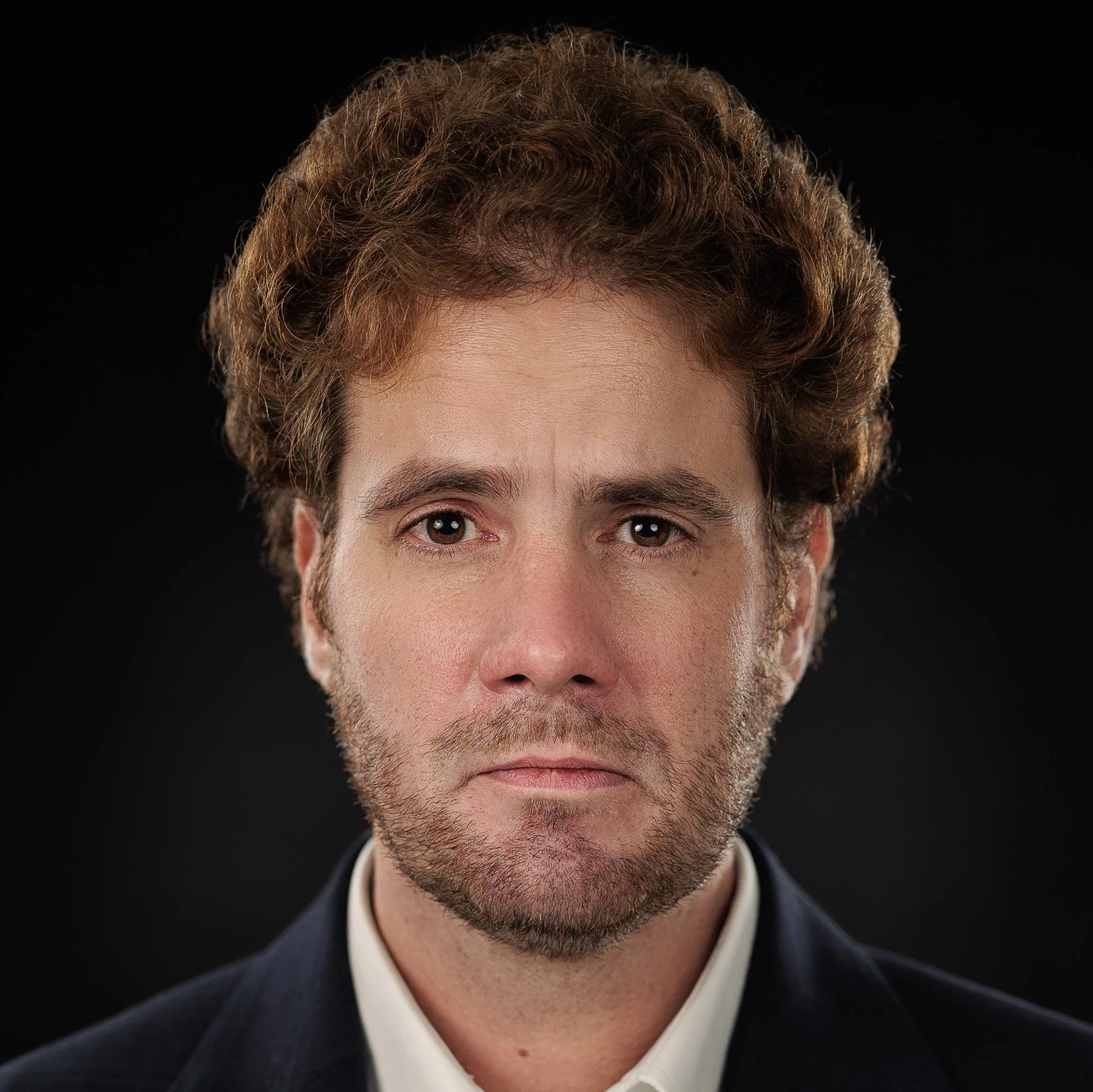 Frontal studio portrait of actor Niccolò Rigutto with direct gaze, wearing a tailored suit, neutral background.