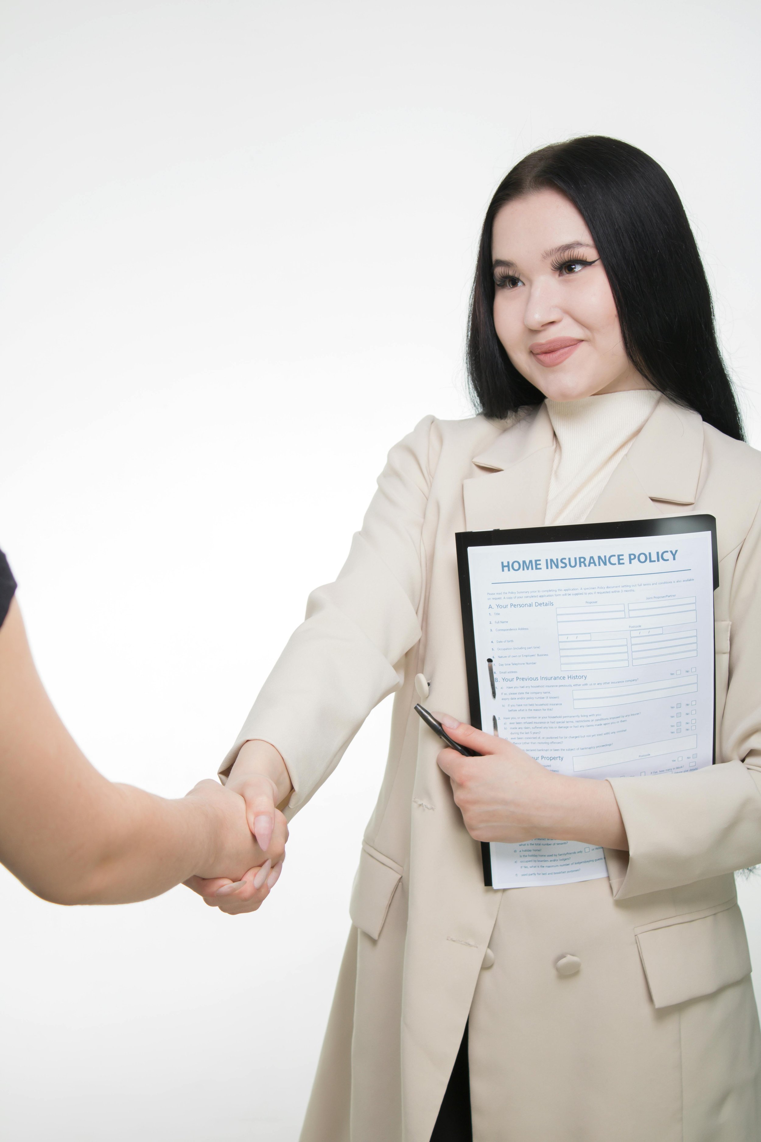 Businesswoman shaking hands while holding a clipboard with a home insurance policy form, smiling.