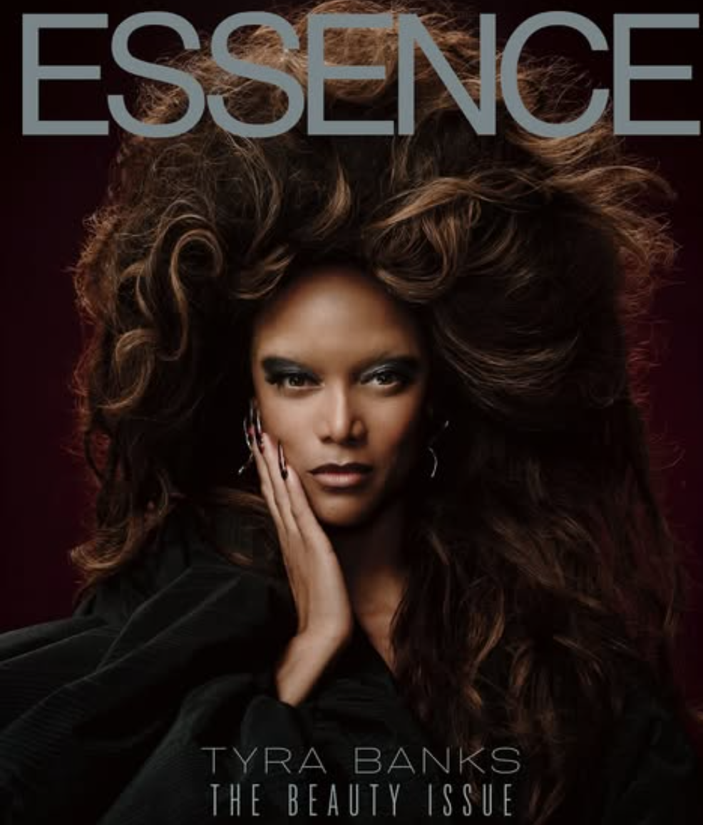 Une femme avec de longs cheveux bouclés, portant des boucles d'oreilles, regardant fixement l'objectif, avec la main sur le visage, sur la couverture d'un magazine intitulé « ESSENCE » avec le texte « TYRA BANKS THE BEAUTY ISSUE ».