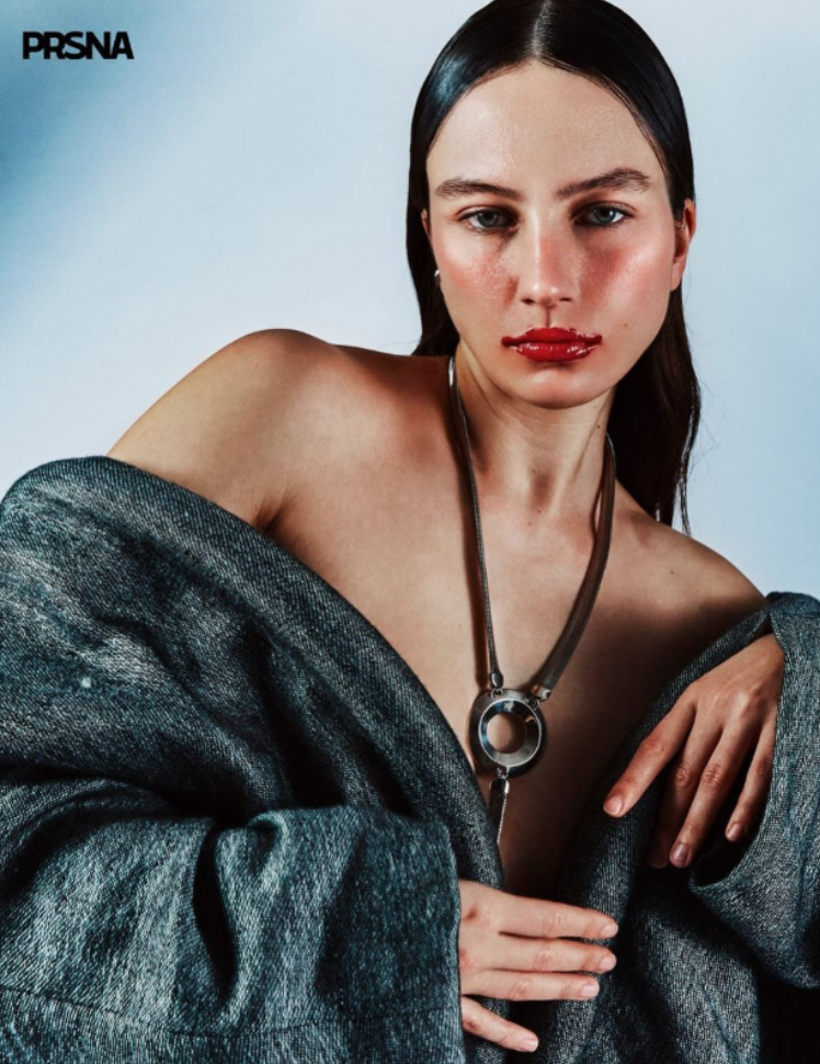 Une femme avec les cheveux bruns longs, portant un manteau gris et un collier métallique