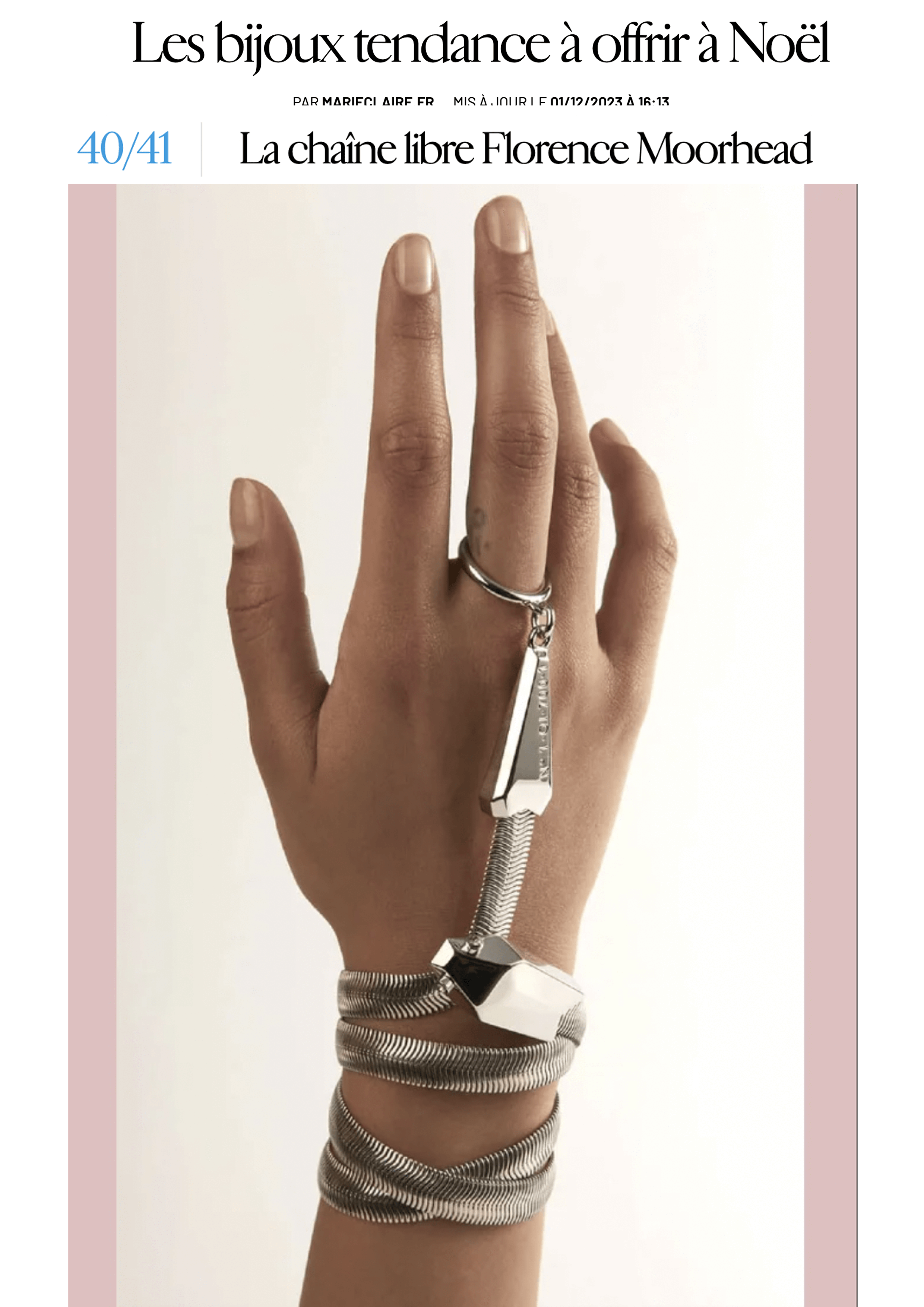 Une main portant un bracelet serpent argenté. La main est levée contre un fond blanc. En haut de l'image, il y a un article de magazine en français intitulé "Les bijoux tendance à offrir à Noël".