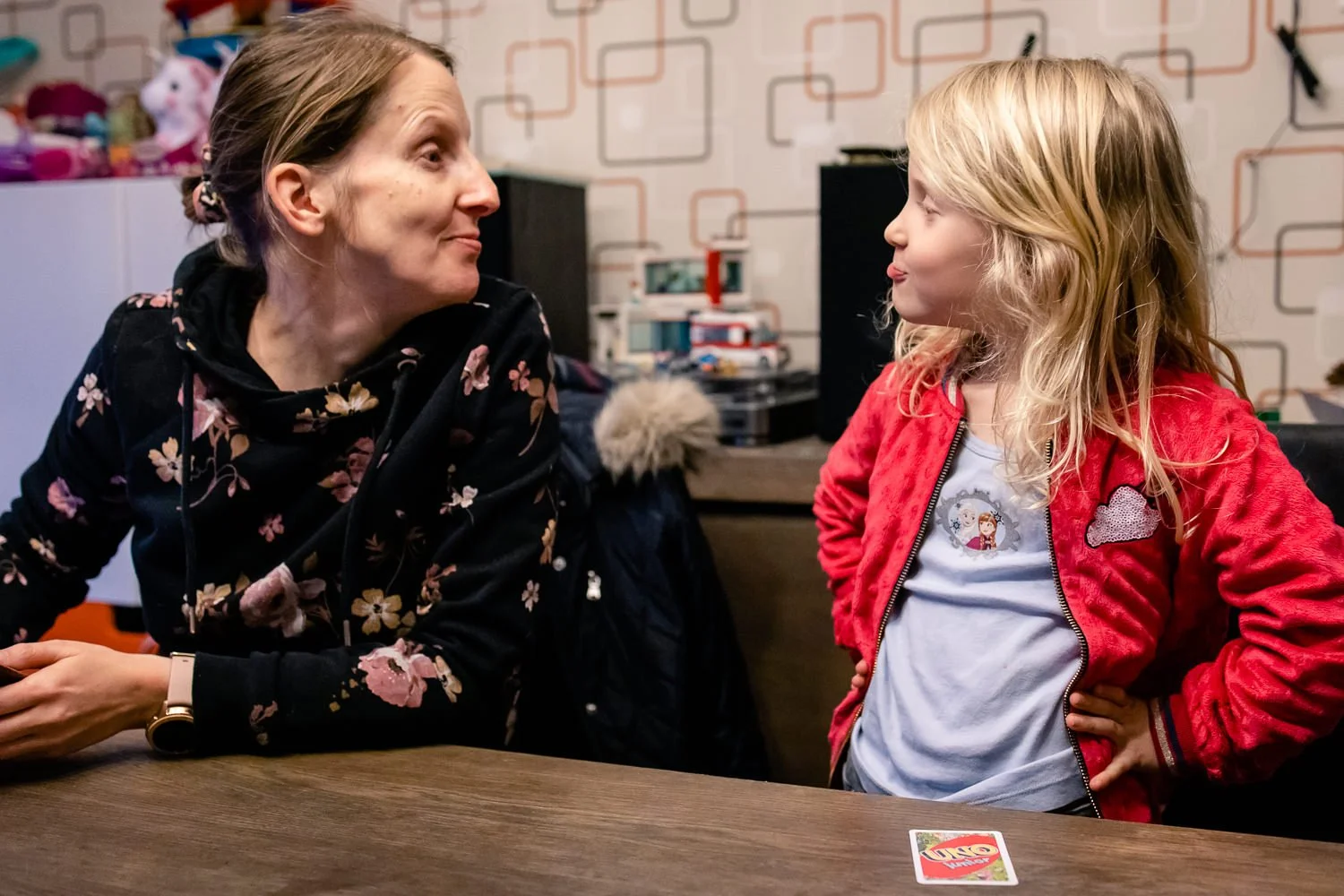 Een vrouw en een meisje kijken elkaar lachend aan, zittend aan een eettafel.