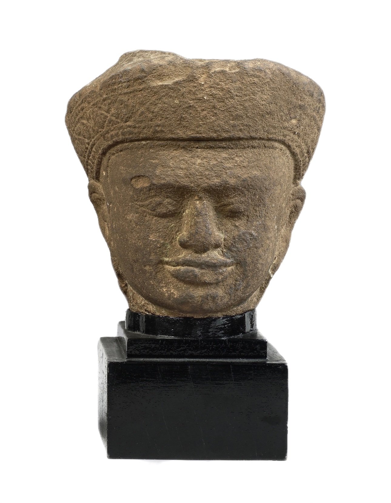 A head of a male deity in beige sandstone. His braided hair in a bun is encircled by a diadem tied at the back. Cambodia, 11-12th Century C.E.