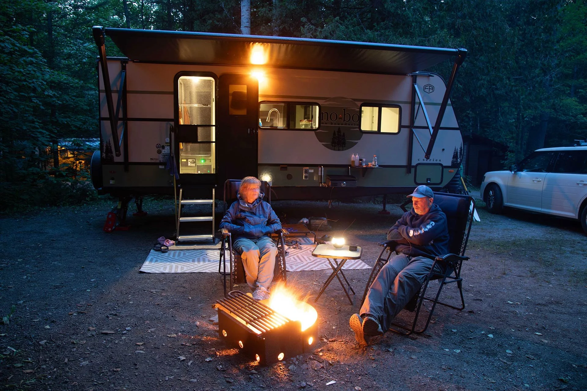Sitting by the campfire with a trailer in the background at an Ontario Provincial Park.