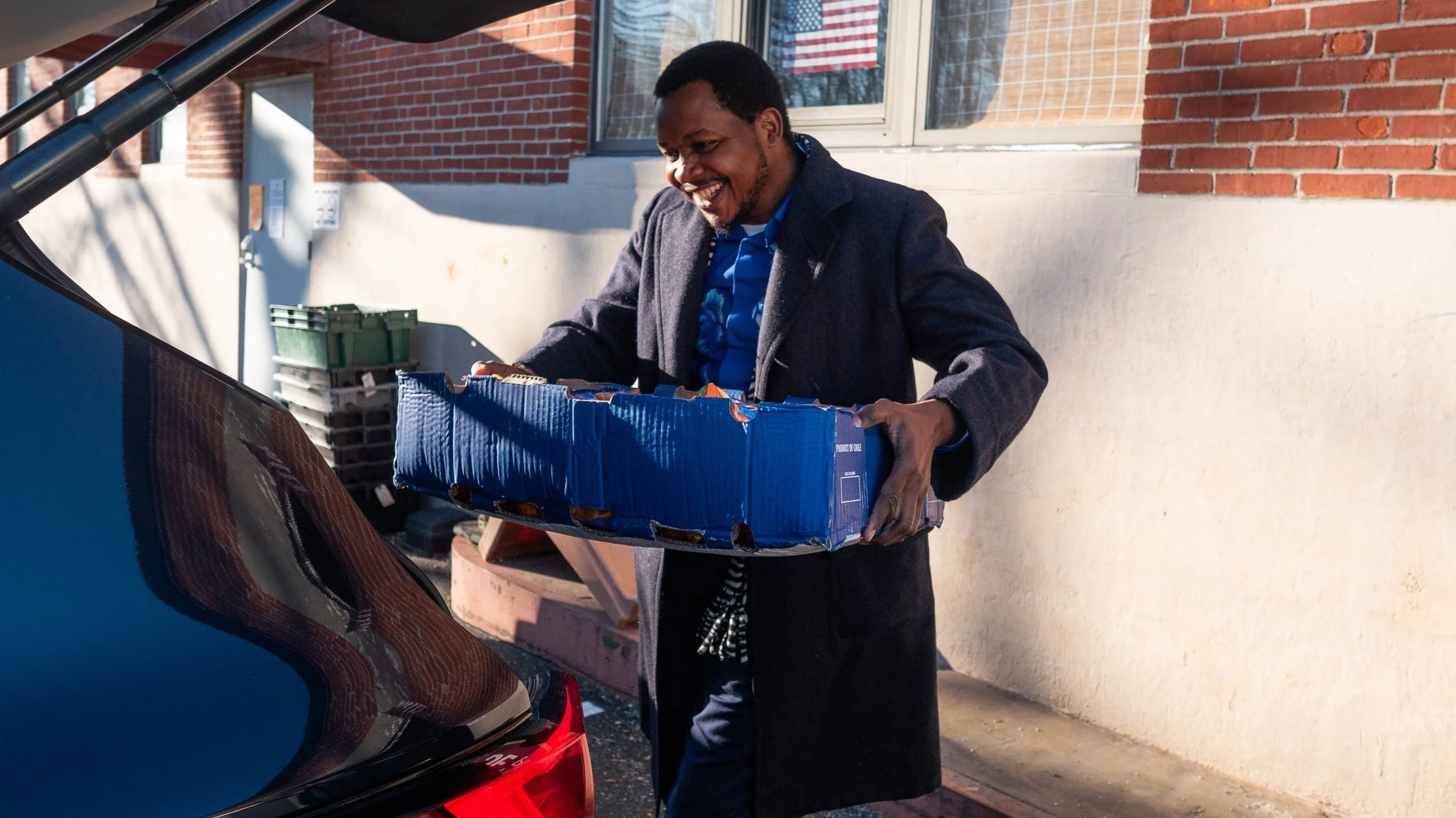 A man loading a box of snacks into a car outside a brick building