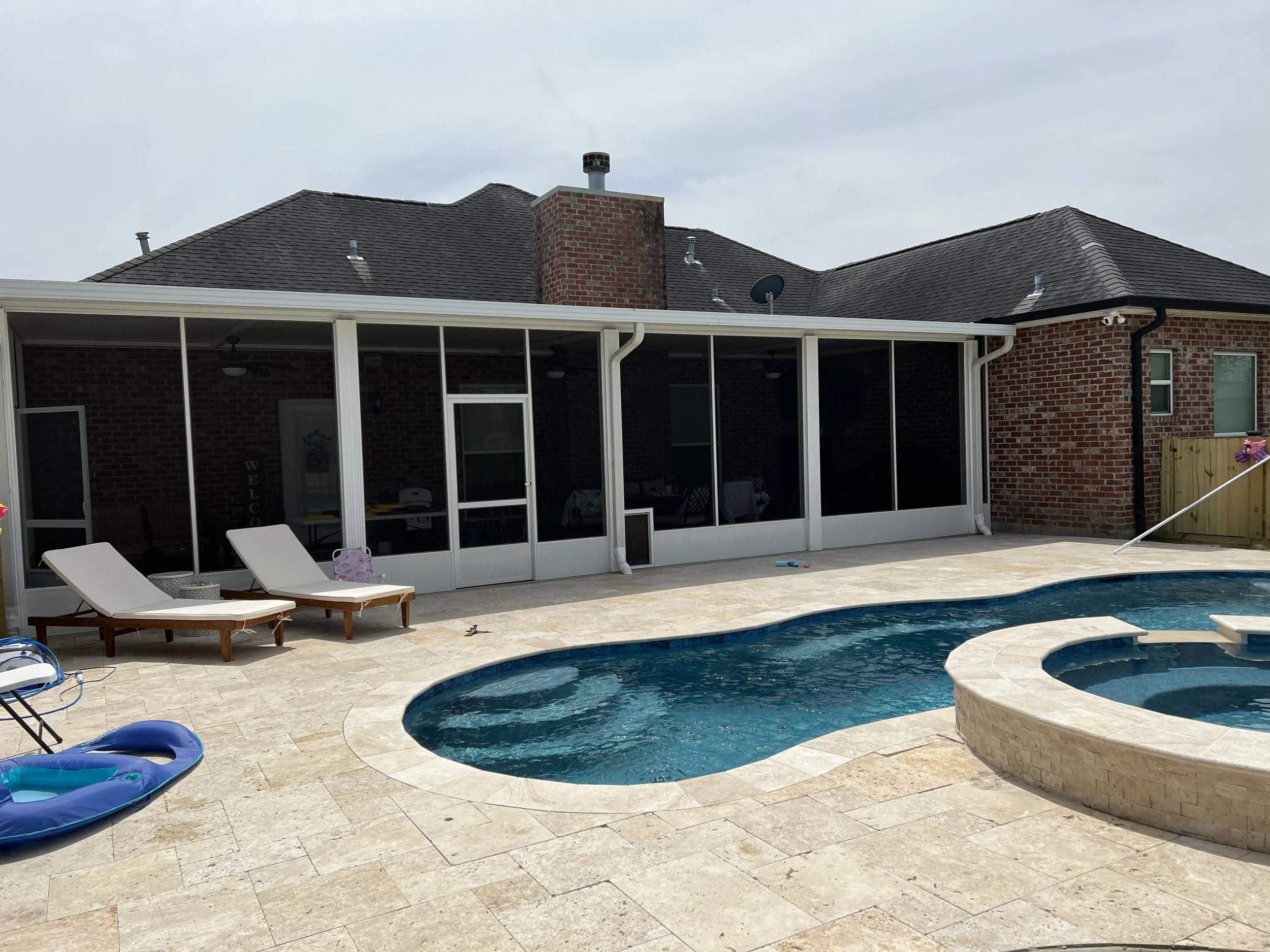 Backyard with a swimming pool, hot tub, two white lounge chairs, and a brick house with large windows.