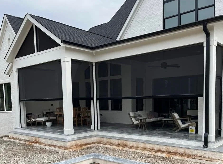 White house exterior with a screened-in patio, featuring outdoor furniture and a ceiling fan, on a tiled floor.