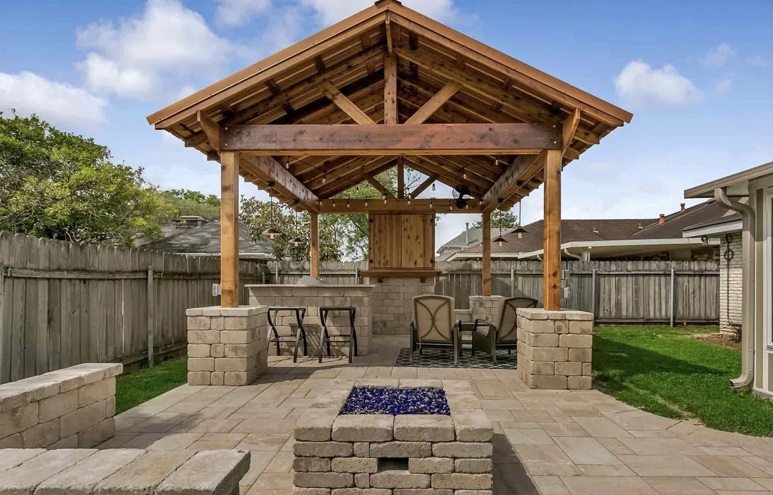 Backyard patio with a wooden pergola, bar area, seating, and stone fire pit