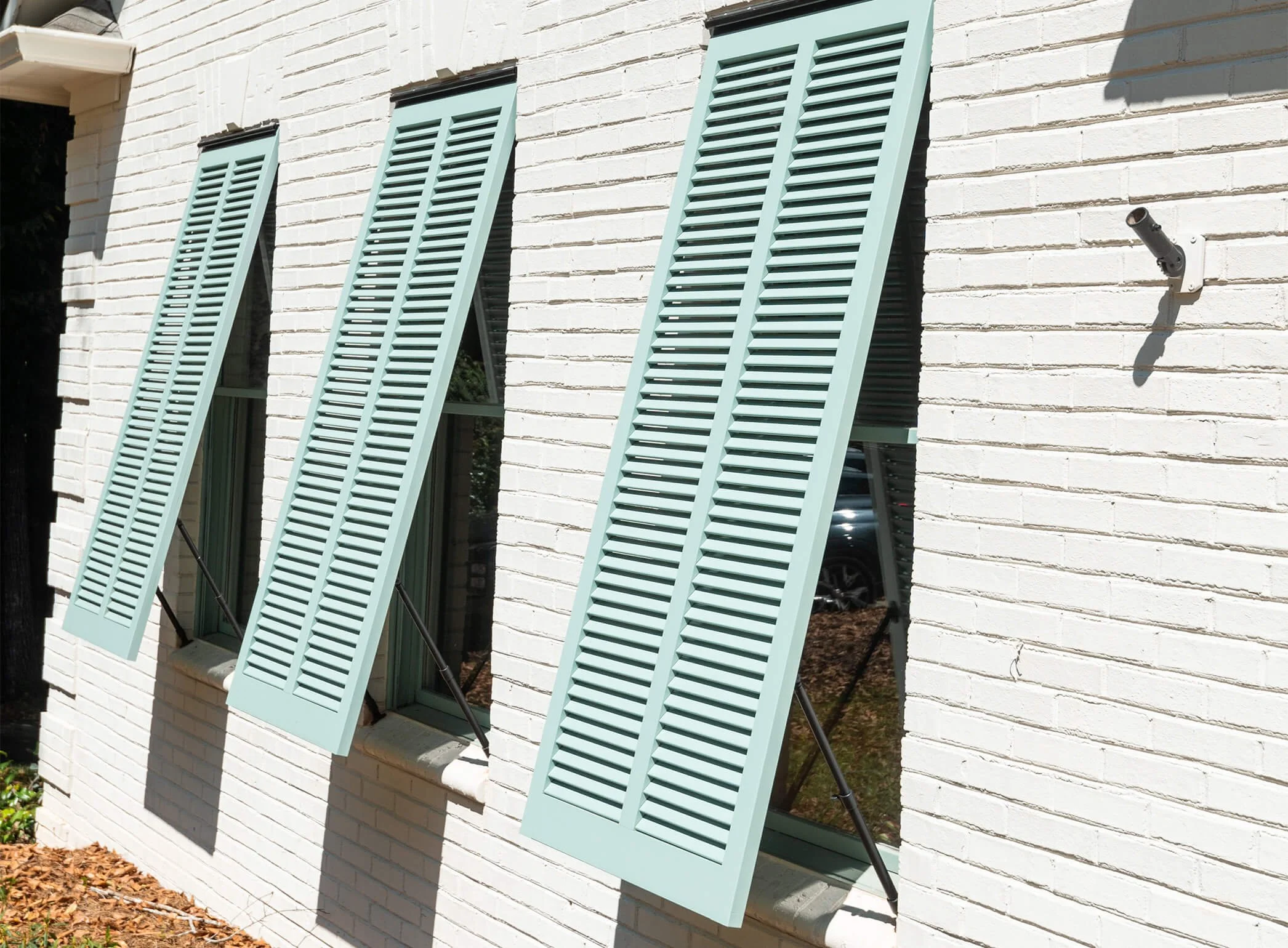 Three light blue exterior shutters partially open on a white brick wall.
