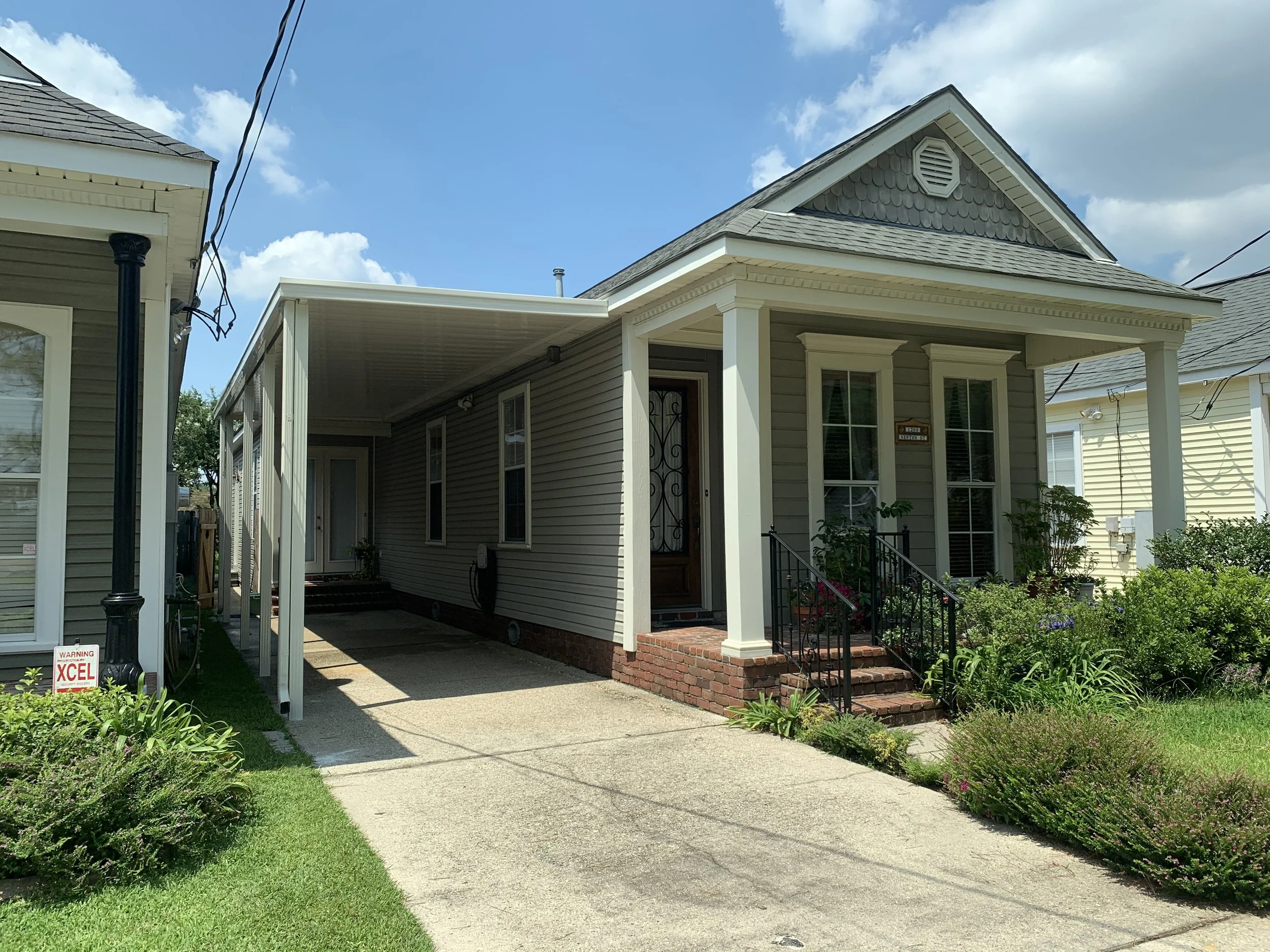 Front view of a small suburban house with a covered driveway, porch with steps, and landscaped garden.