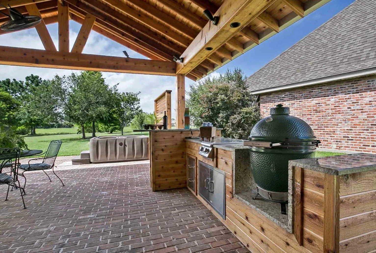 Outdoor patio with a barbecue grill, brick flooring, wooden pergola, and seating area overlooking a grassy yard.