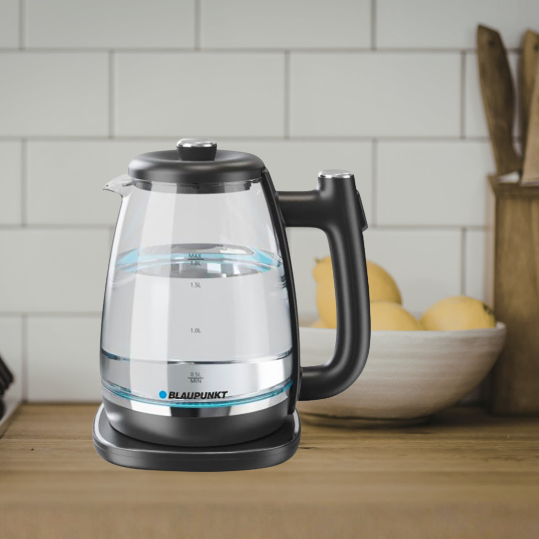 Elektrische waterkoker op een houten keukenblad, met een witte tegel muur en een kom met gele vruchten op de achtergrond.