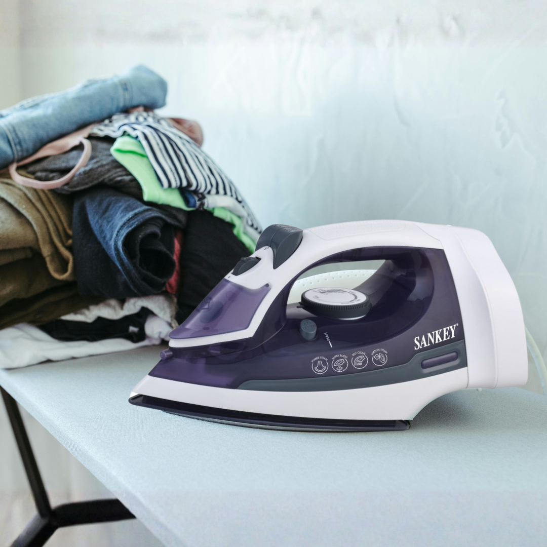 Een strijkijzer op een tafel met opgevouwen kleding op de achtergrond.