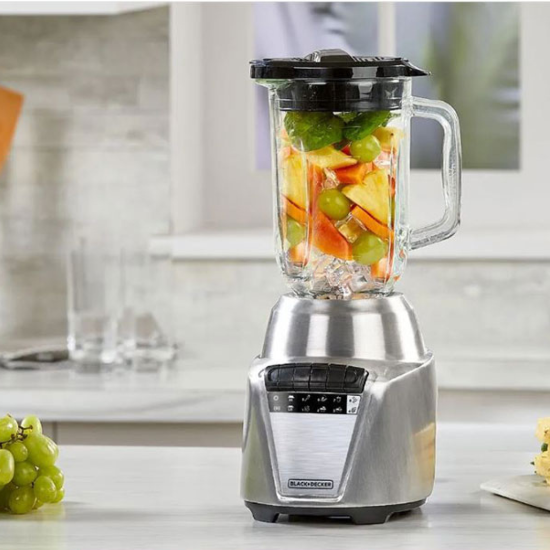 Blender met gemengde vruchten, waaronder groene druiven, appels, en ananas, in een keuken.