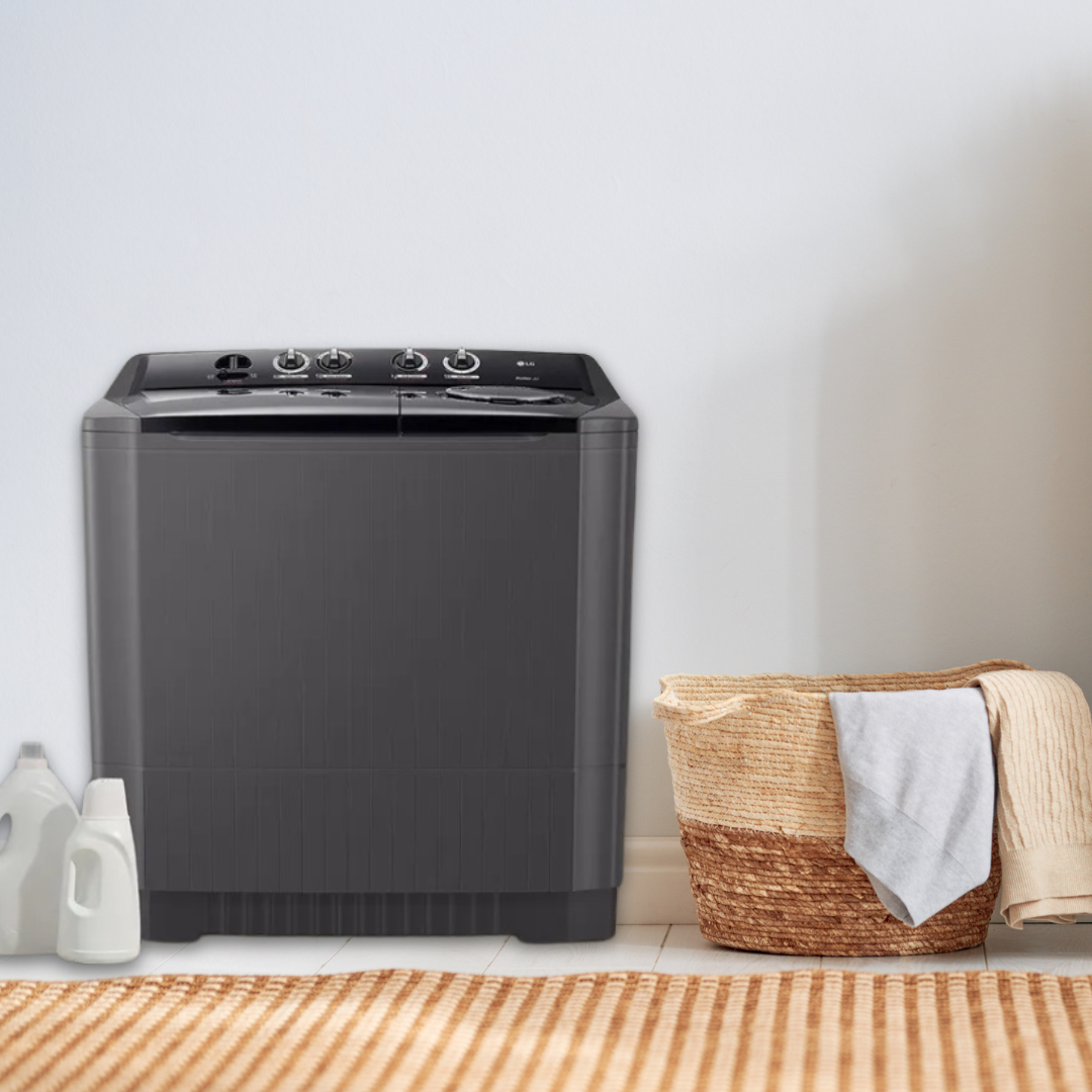 Een wasmachine naast een wasmand met kleding en wasmiddelen op de vloer.