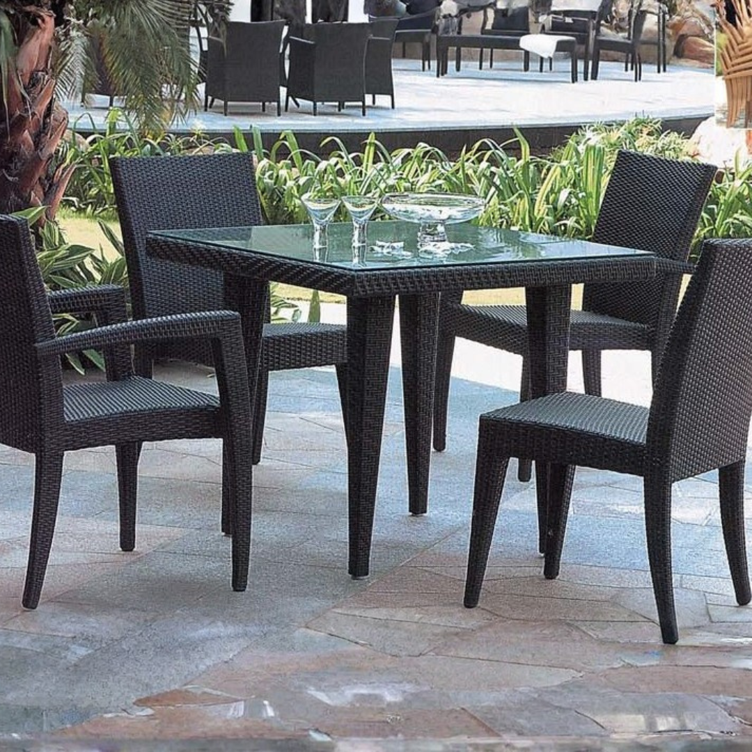 Buiten tafel met vier zwarte wicker stoelen en glazen met drankjes en bloemen in een vaas.