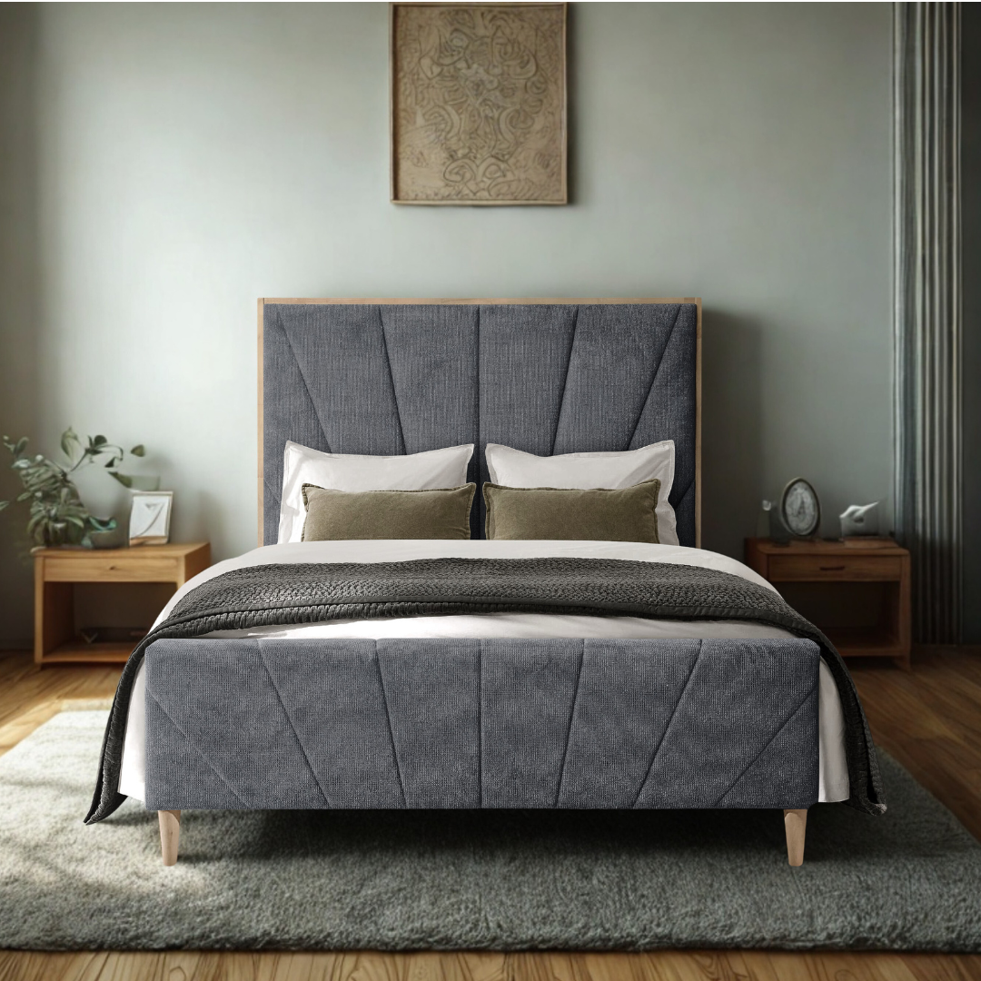 Een slaapkamer met een bed dat een grijs hoofdbord heeft en wit en groene kussens, met nachtkastjes aan beide zijden. Op de linkernachtkastje staan planten en een foto, op de rechter een klok en een klok en een witte mouw. Er hangt een kunstwerk boven het bed en het kamer heeft een houten vloer.