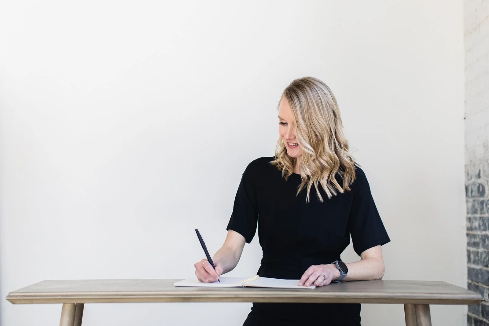 Lauren Payne wellness coach, a smiling blonde woman looks down at a notebook she is writing in