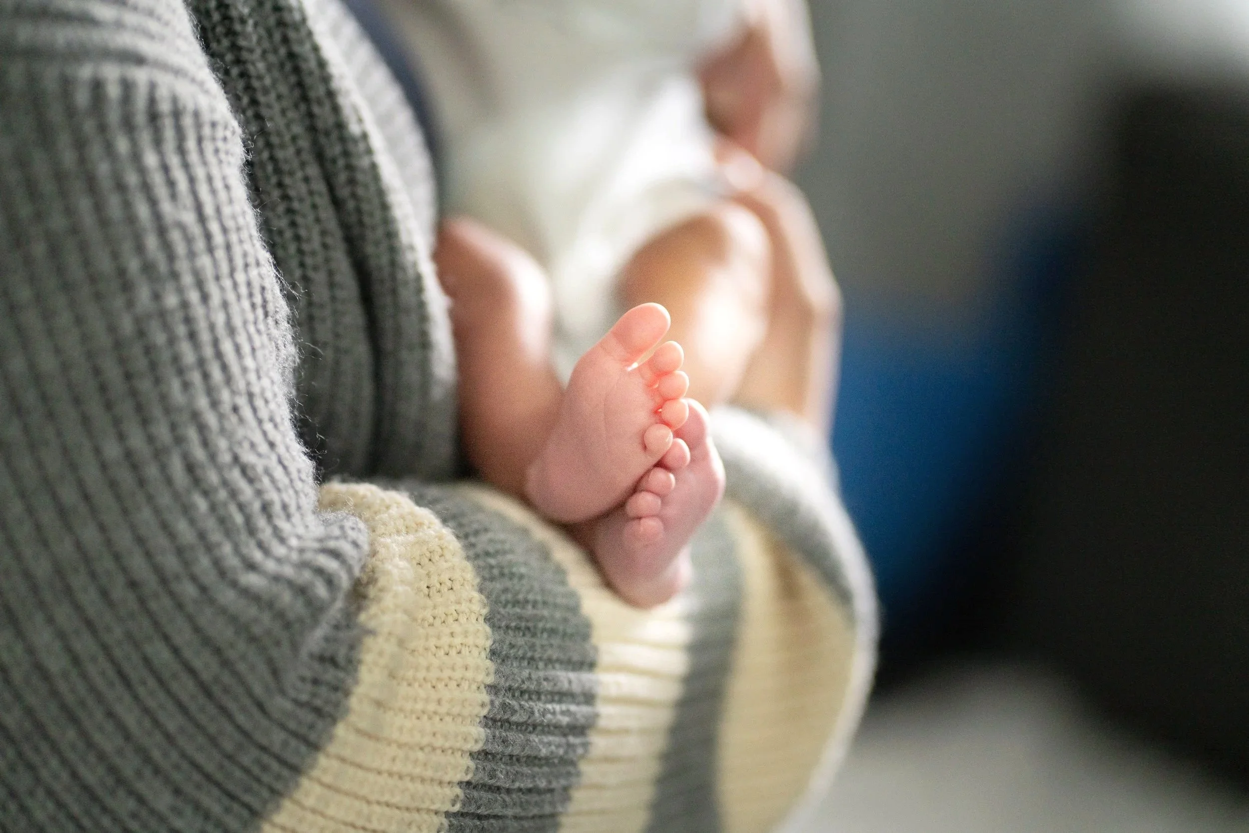 Close-up of a person's hand showing their fingers, with another hand and fingers blurred in the background. The person is wearing a striped sweater.