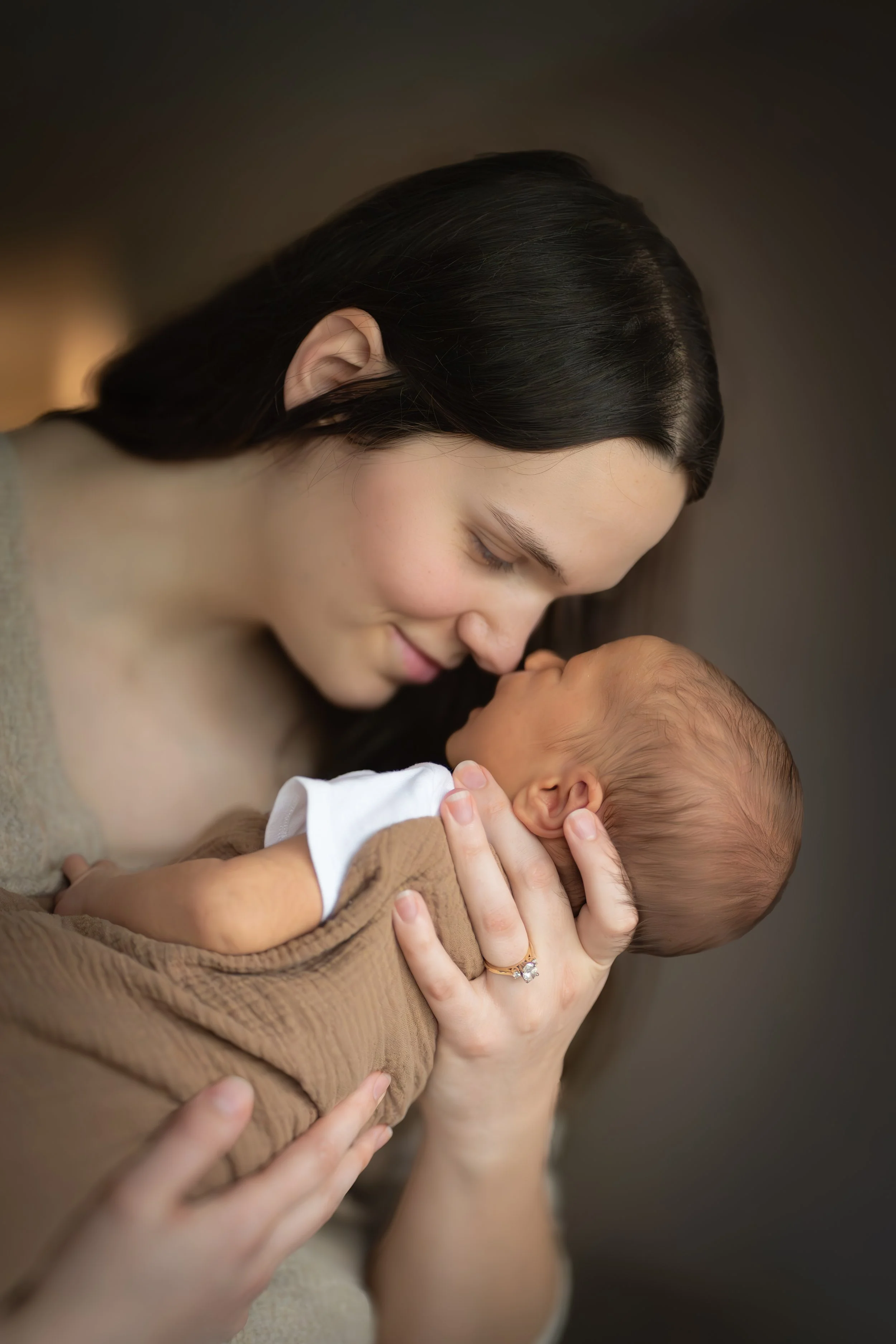 A woman with dark hair gently holding a newborn baby close to her face, her eyes closed, in a tender moment.