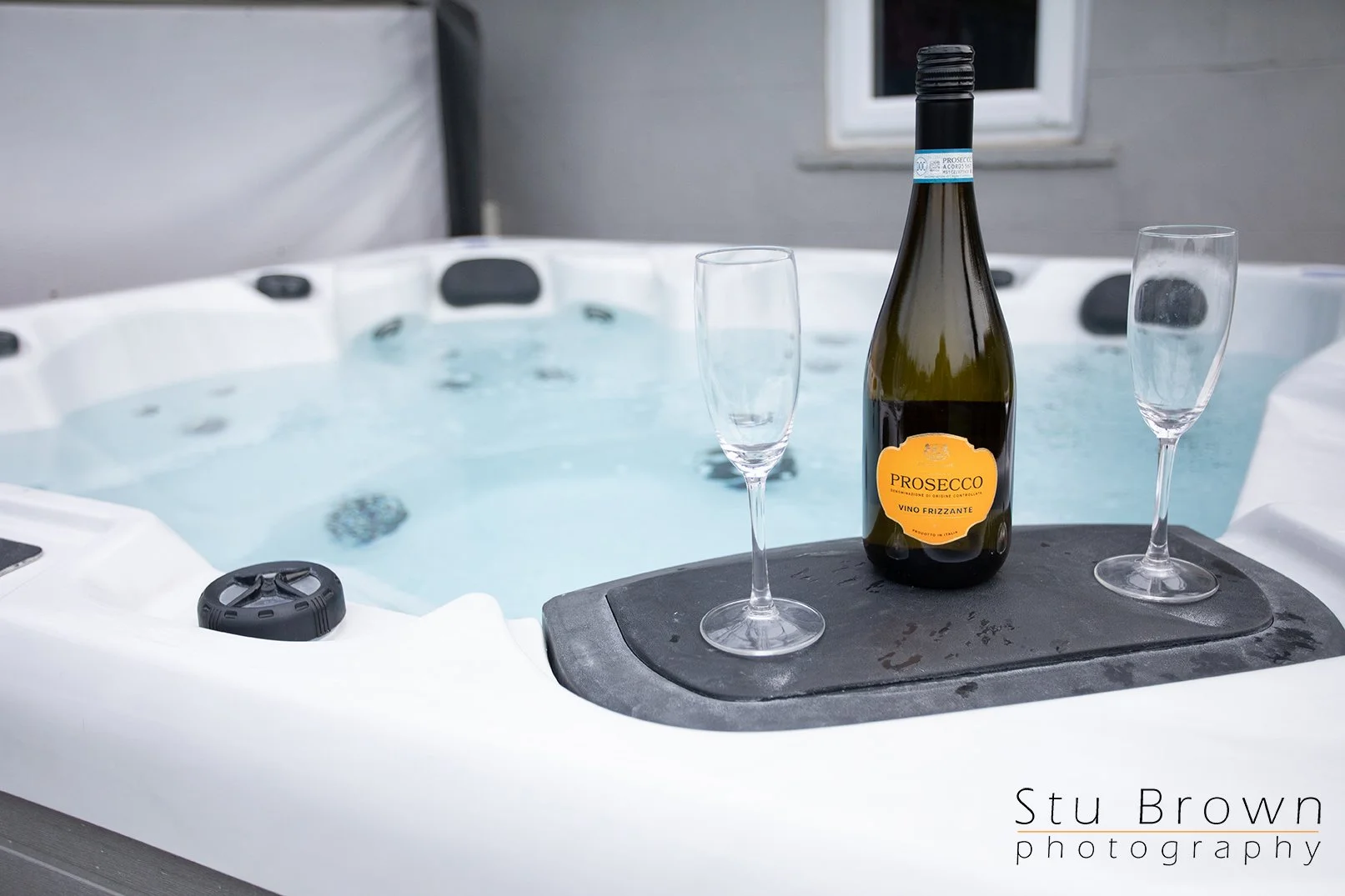 A hot tub with a bottle of Prosecco and two empty champagne flutes on the edge of the tub.