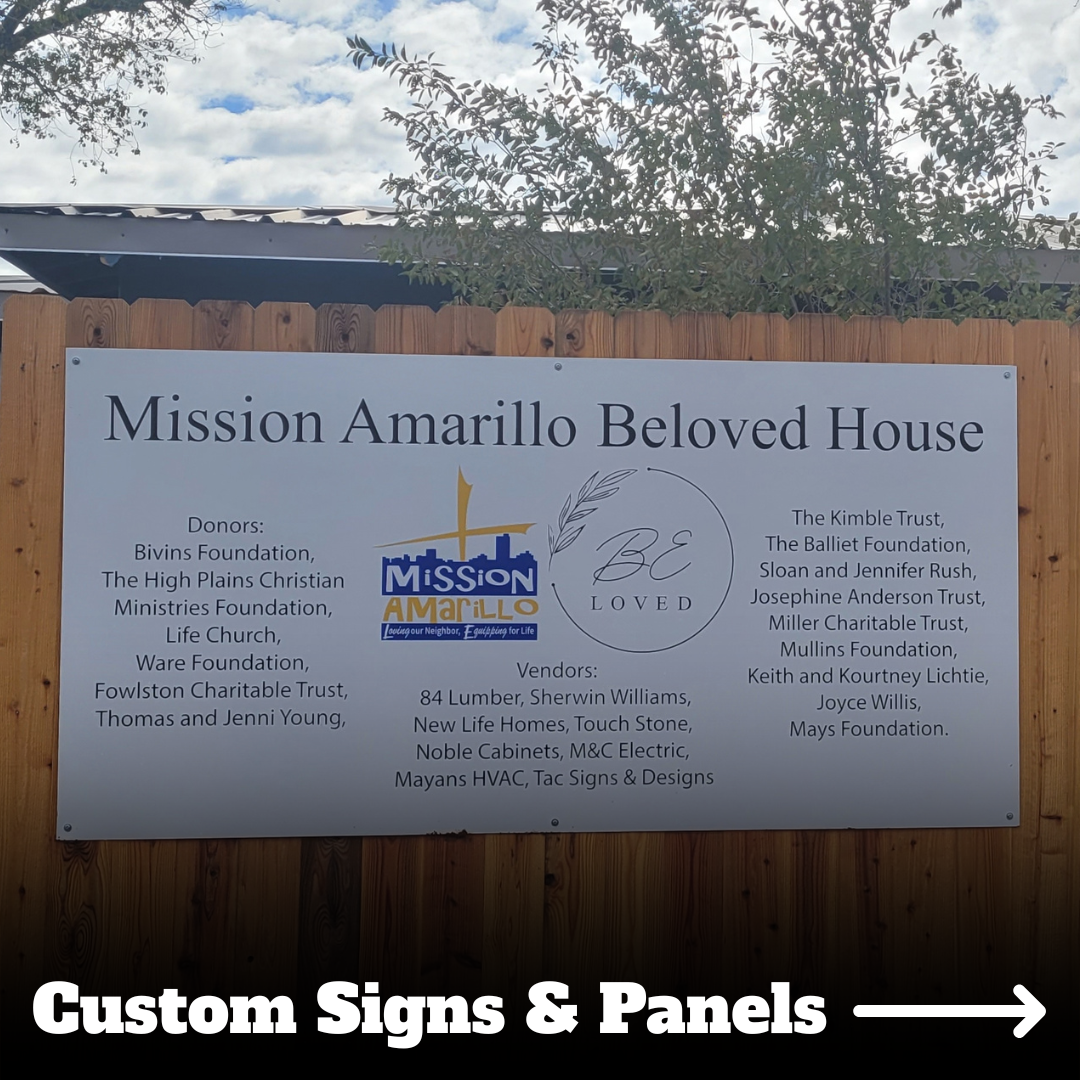 A large wooden fence with a metal sign attached. The sign reads 'Mission Amarillo Beloved House' with logos, donors, and vendors listed below. The sky is partly cloudy with trees visible in the background.