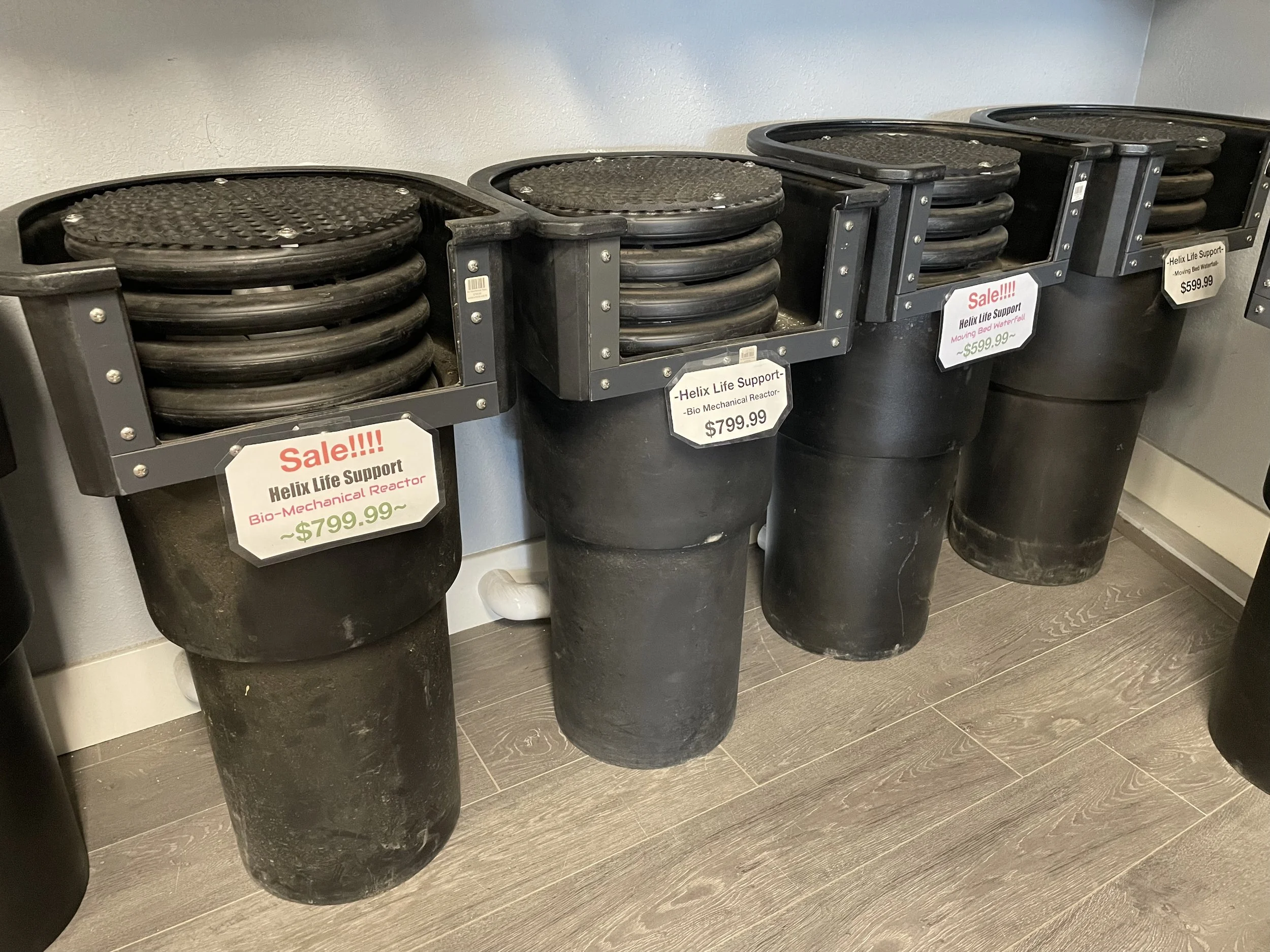 Display of black plastic bins containing black rubber rings, with sale signs advertising Helix Life Support Bio Mechanical Reactor priced at $799.99 and $599.99.