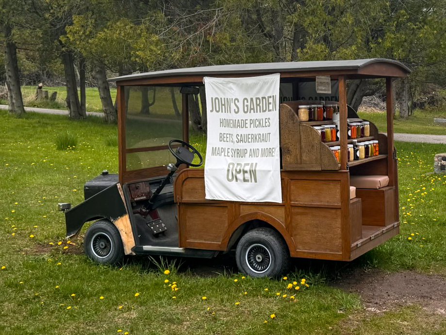 The side of John’s Garden farm stand on Washington Island, Wisconsin, with a large “OPEN” banner attached to the wood-paneled golf cart.