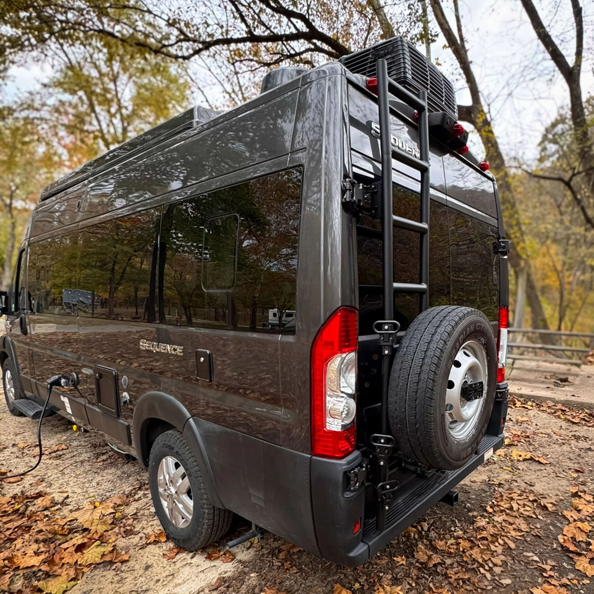 A ladder and spare tire are mounted to the back door of a Ram ProMaster camper van.