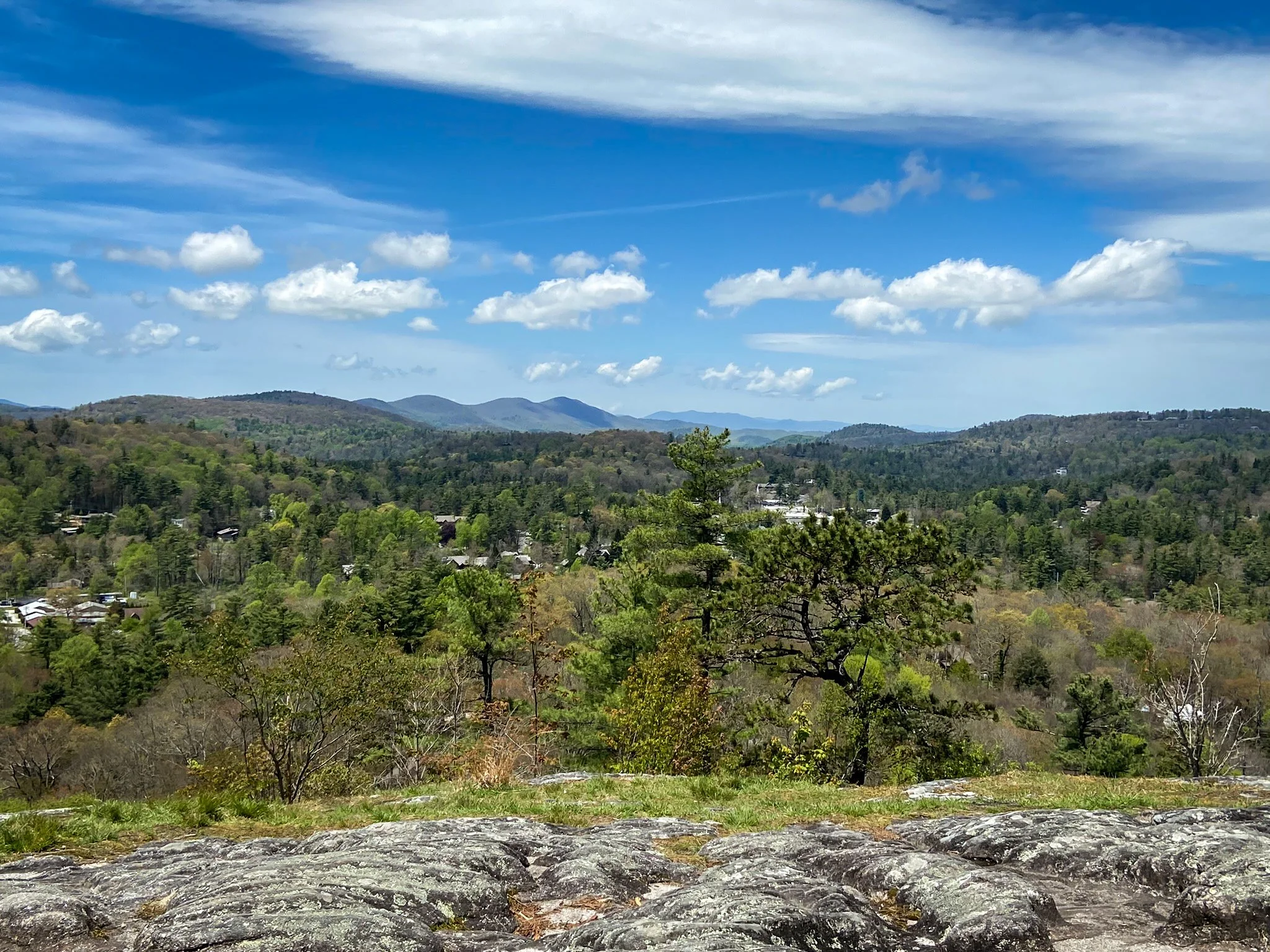 View from Sunset Rock overlooking Highlands, North Carolina, with forested Blue Ridge Mountains stretching into the distance under a clear sky.