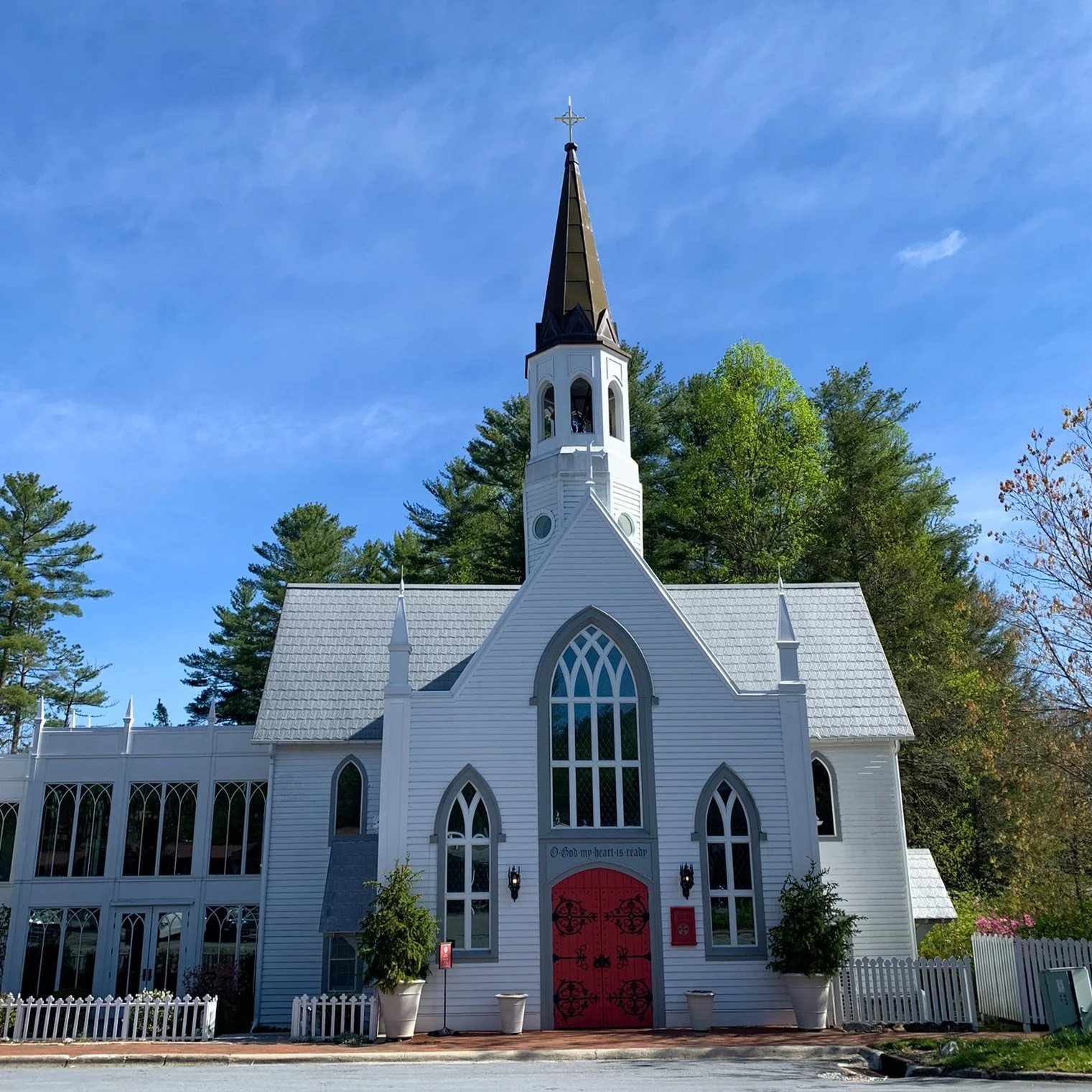 The white-walled Church of the Incarnation in Highlands, North Carolina, gives storybook vibes with its red door, lancet windows, roof finials and circular bell tower.