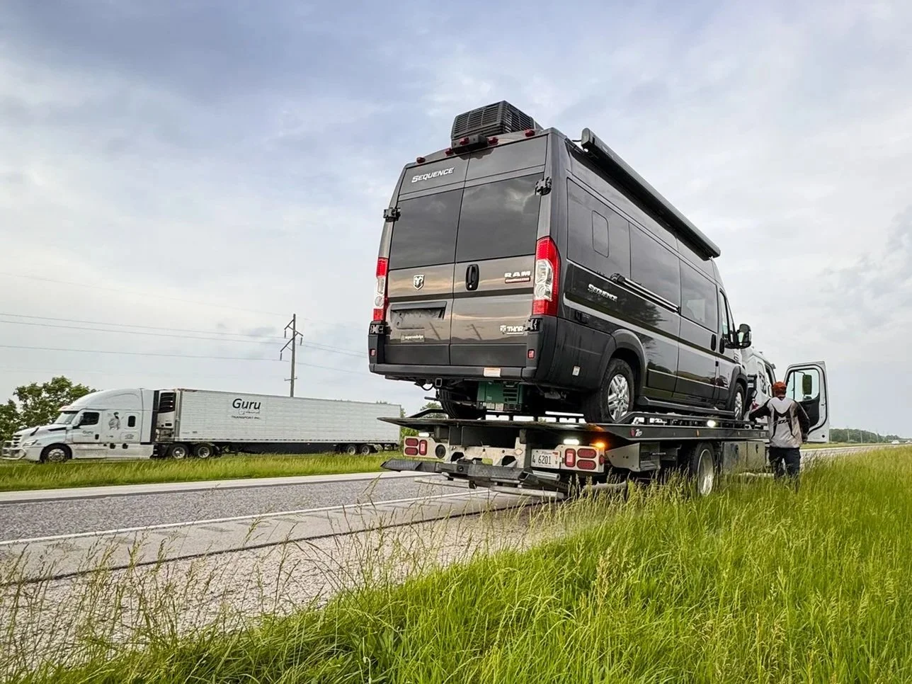 A camper van is loaded onto a tow-truck bed on the side of a freeway in Illinois.