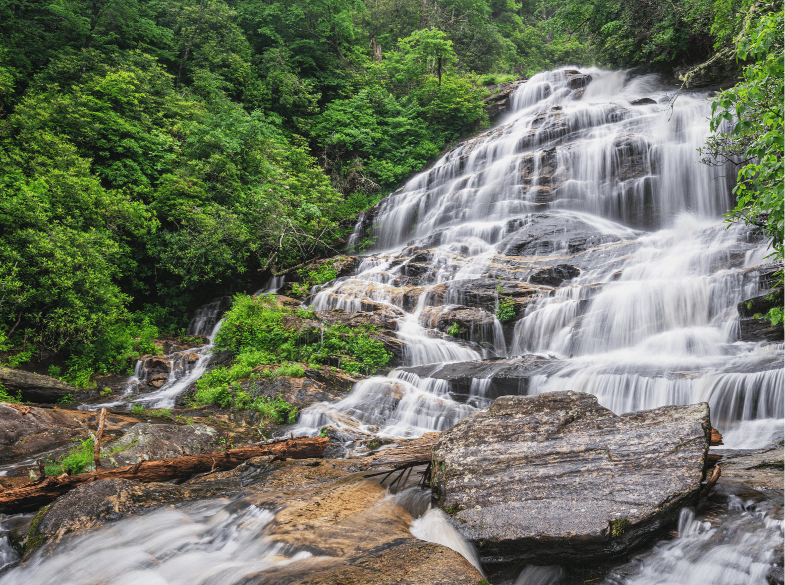 Water cascades over large rocks amid a forested mountain landscape at Glen Falls near Highlands, North Carolina.