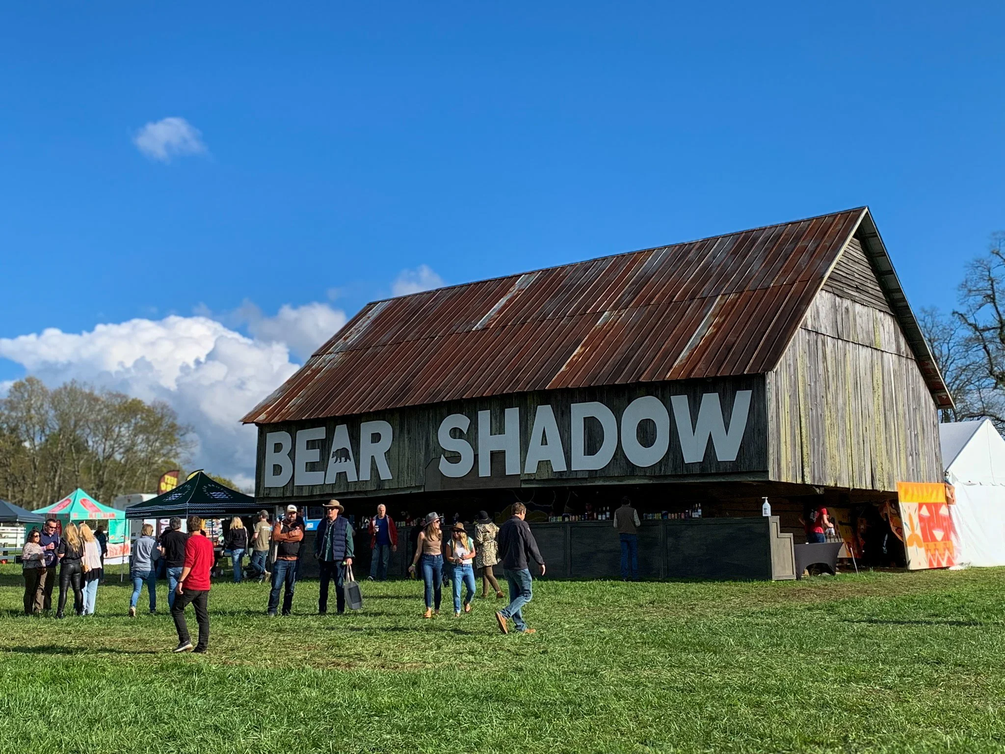 Music festival goers in Highlands, North Carolina, walk in front of a rustic barn with “Bear Shadow” painted across the side.