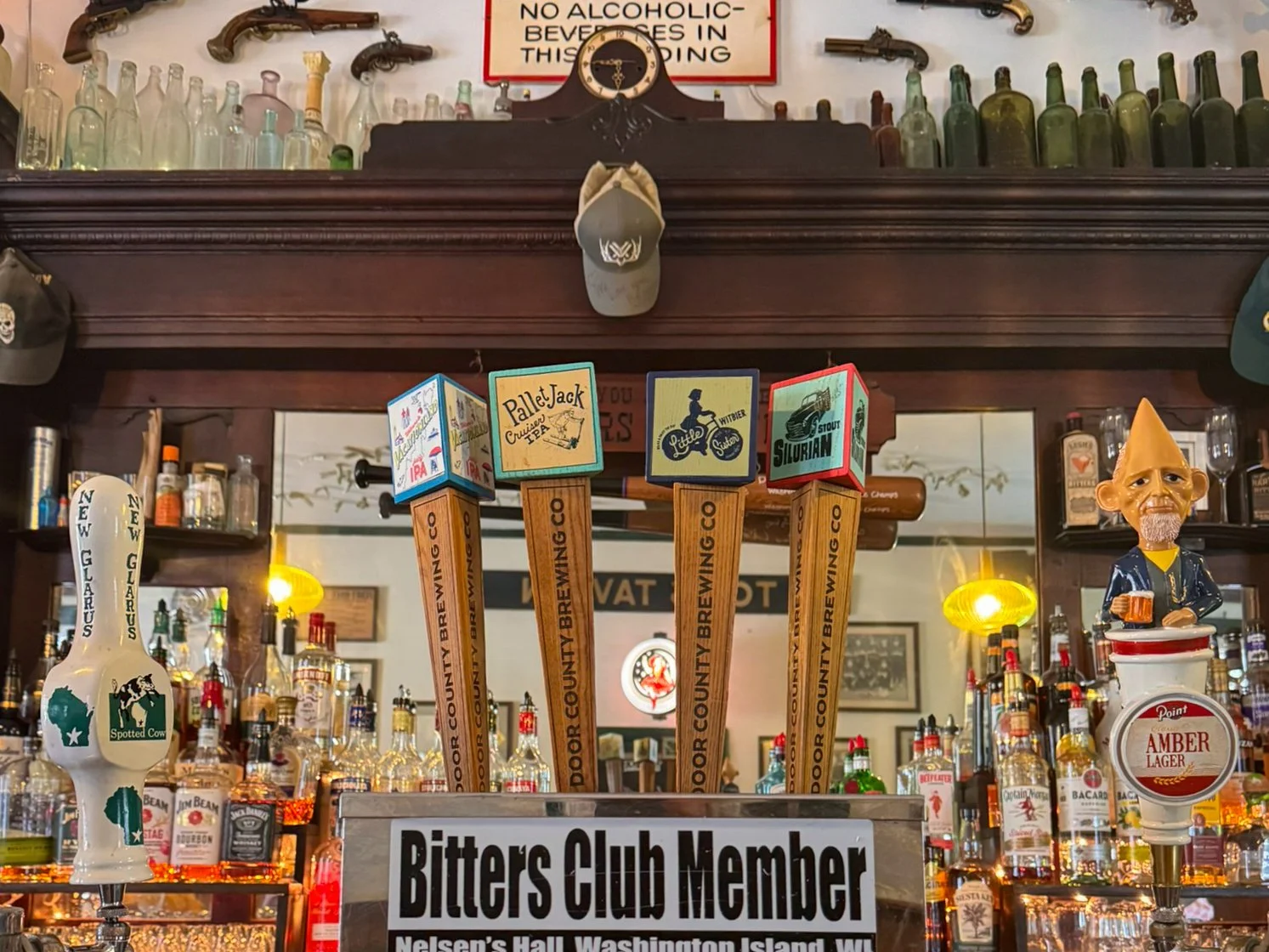 The bar at Nelsen’s Hall on Washington Island, Wisconsin, with draft taps from Door County Brewing Co. and New Glarus Brewing Co., a vintage wooden bar back and mounted guns and memorabilia on the wall.