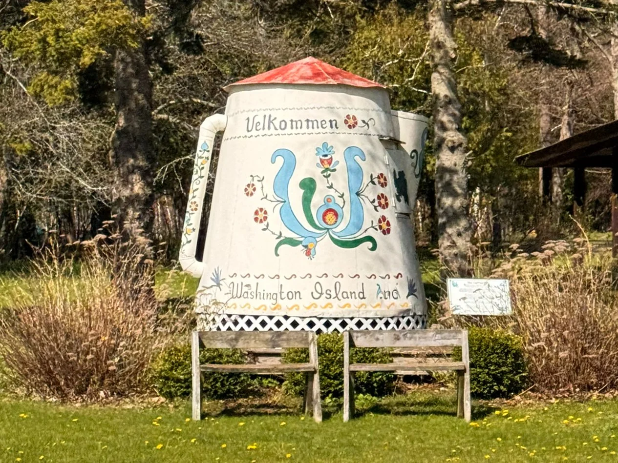 A giant galvanized-steel coffee pot on wheels on Washington Island, Wisconsin, decorated with colorful Norwegian rosemaling and the word “Velkommen” on its side.