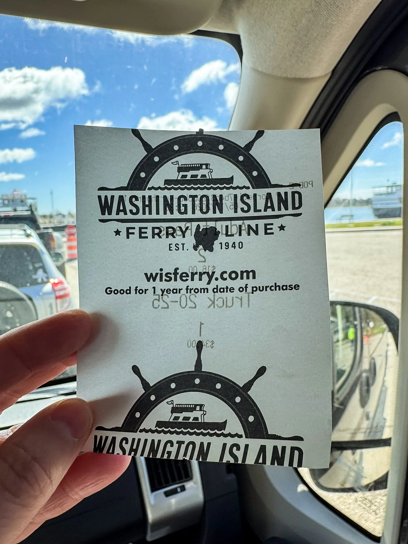 Inside a camper van, a hand holds a Washington Island Ferry ticket. A line of cars waits to board the ferry back to the Door County Peninsula.