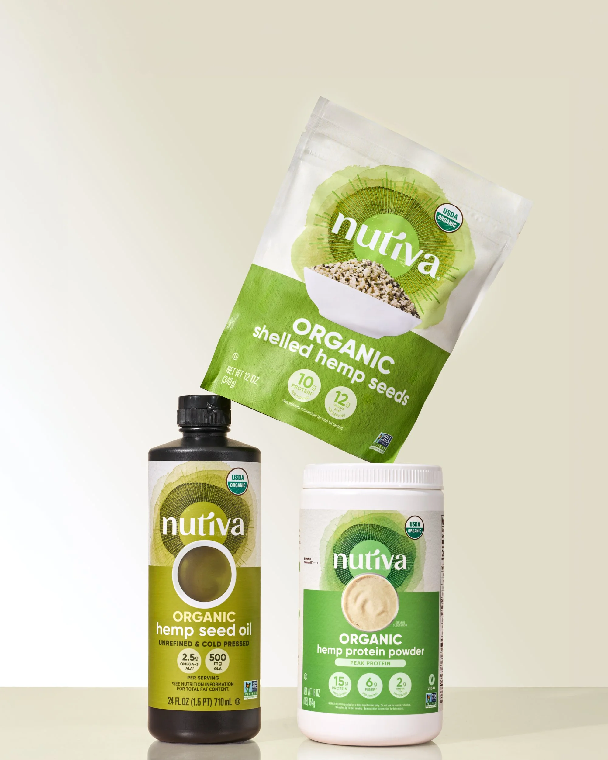 Three Nutiva organic hemp seed products: shelled hemp seeds in a bag, hemp seed oil in a bottle, and hemp protein powder in a container.